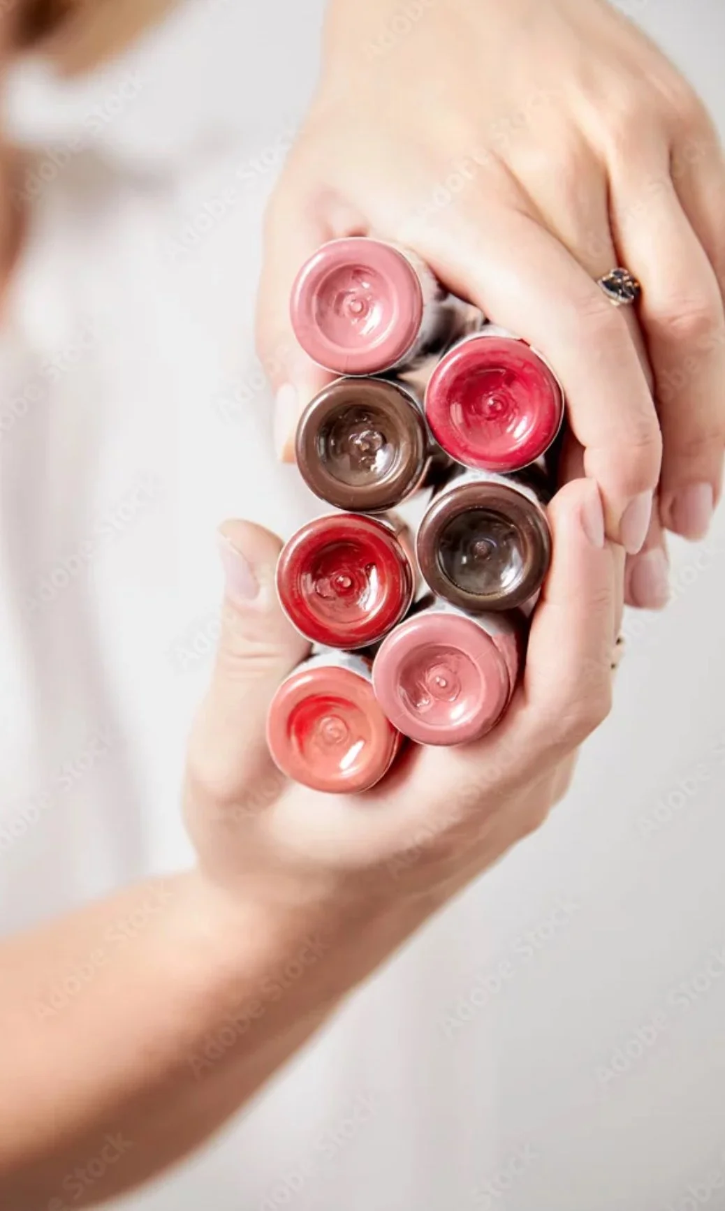 A person holding multiple pmu pigment tubes with the open ends facing up, showing various shades of pink and brown.