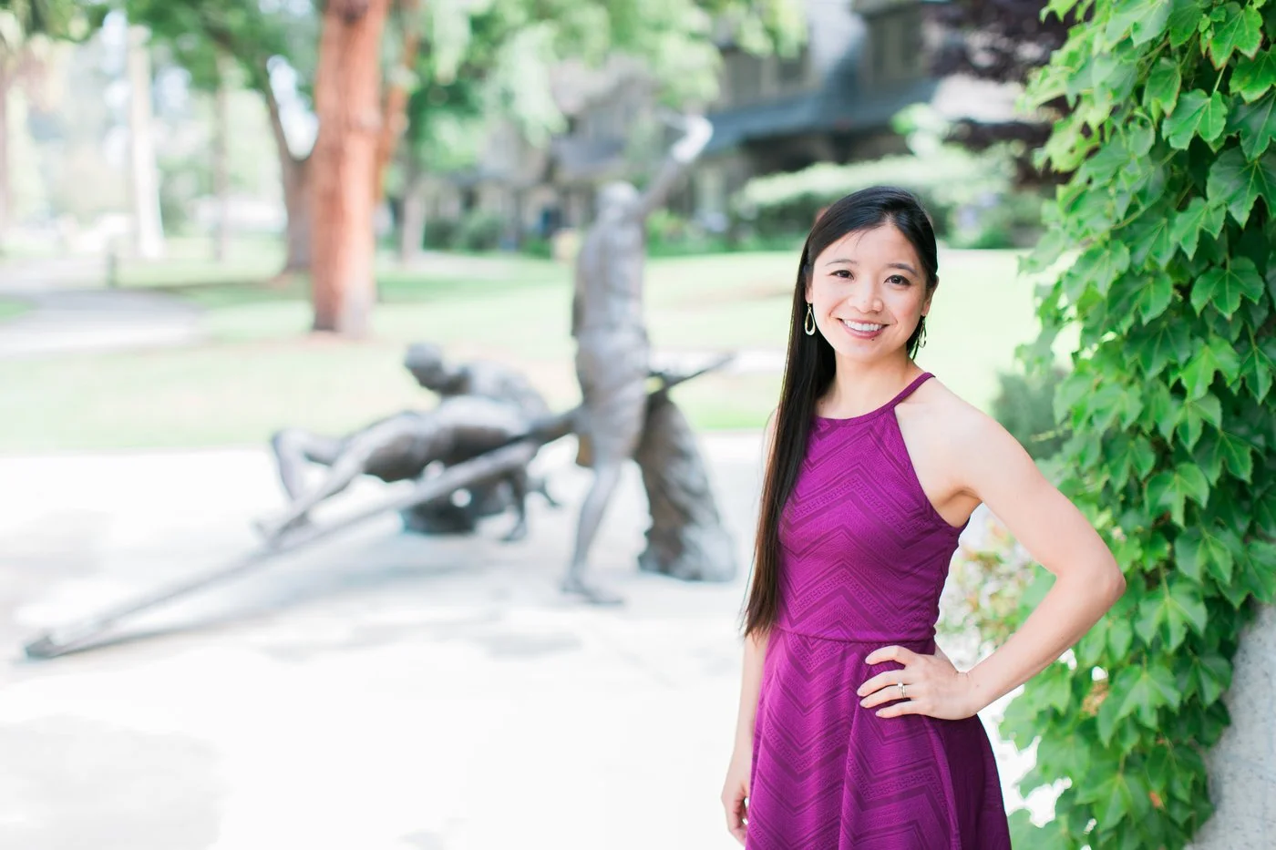 Grace Ou, LMFT, a therapist offering counseling in Los Angeles, CA, standing outdoors in a park beside a wall of green ivy with a blurred sculpture in the background.