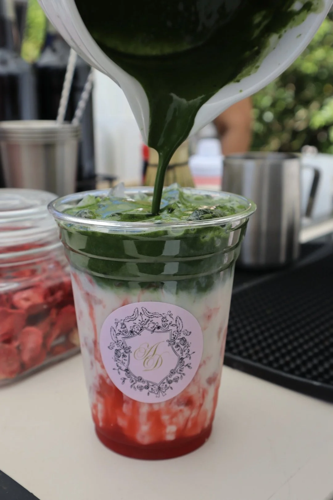 Bascota pouring freshly whisked matcha into a strawberry matcha latte with layered strawberry and matcha colors at a private bridal shower. 