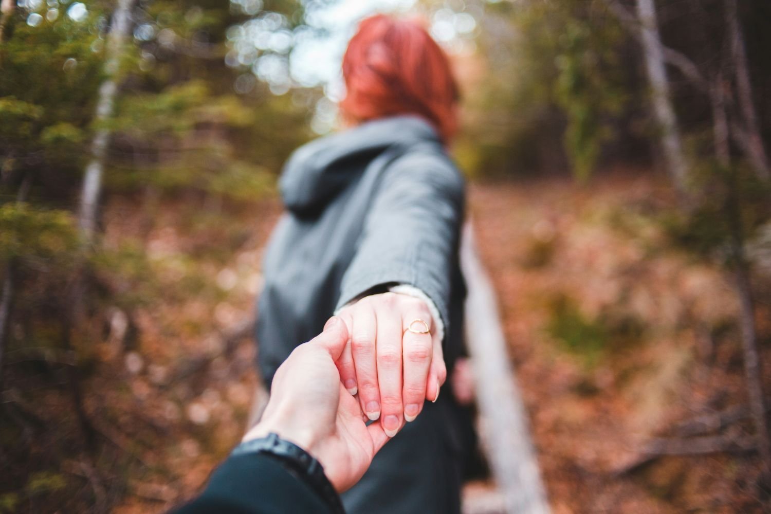 Woman holding a person's hand while walking away into a forest.