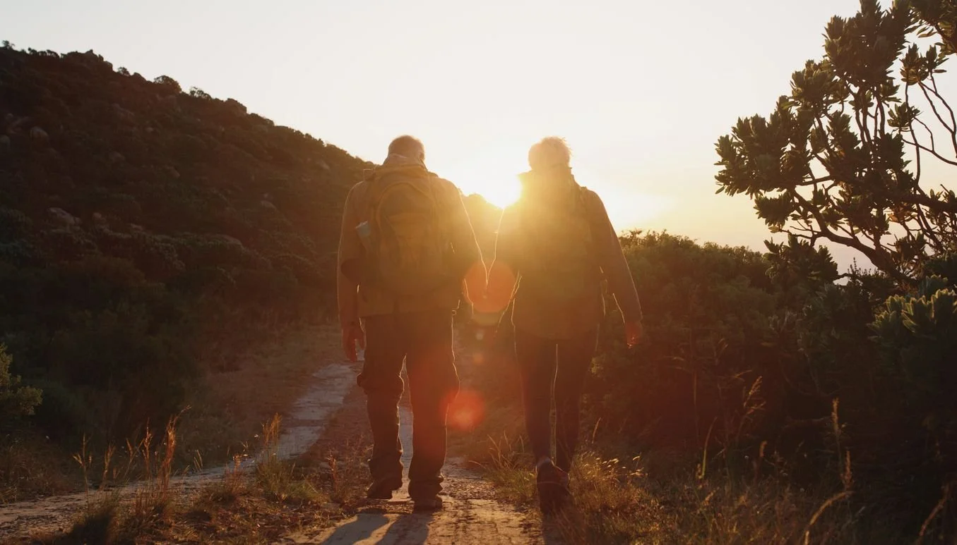 Photo of two people holding hands while walking on a trail in a desert.