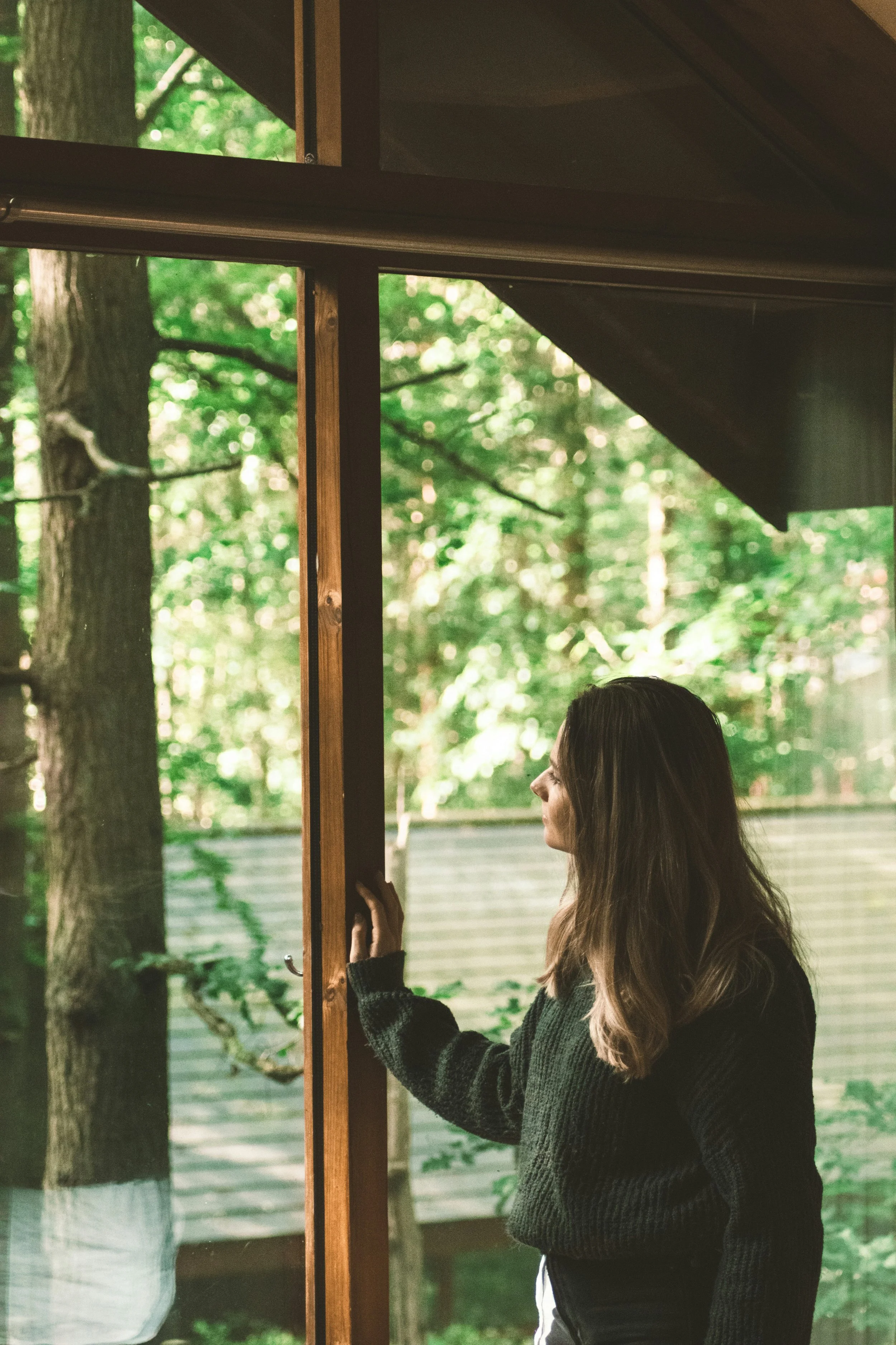 Woman looking out a window at a forested backyard