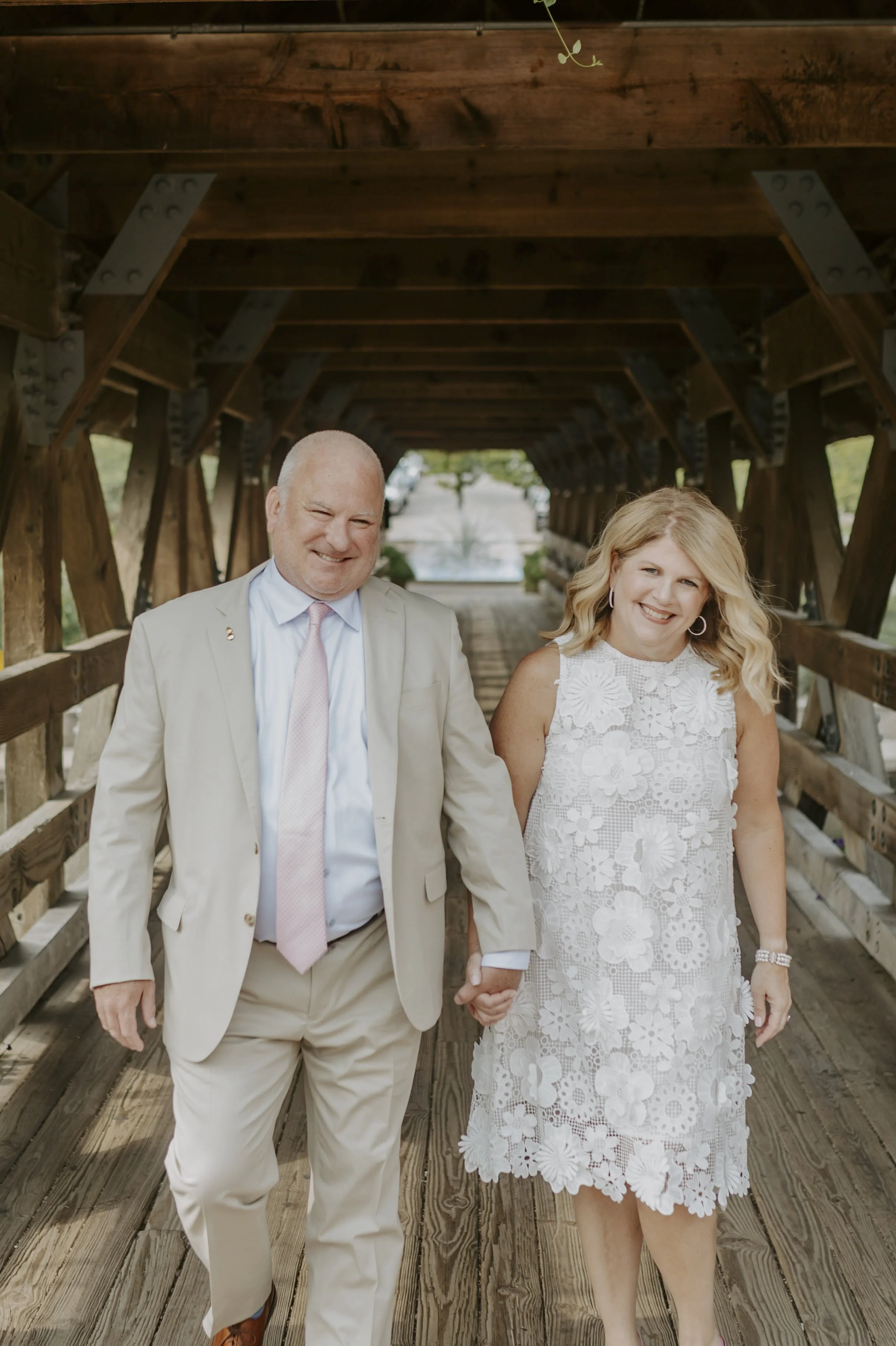 A bride and groom walk down a covered bridge