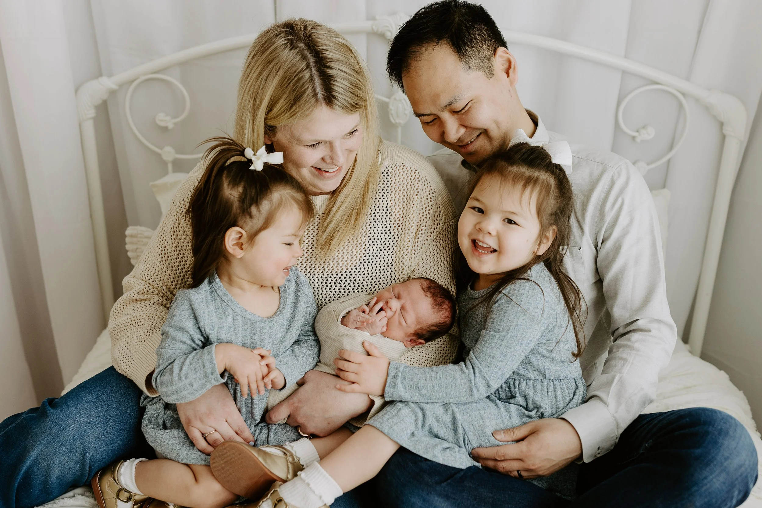 A family of five sits on a bed and snuggles the newborn baby