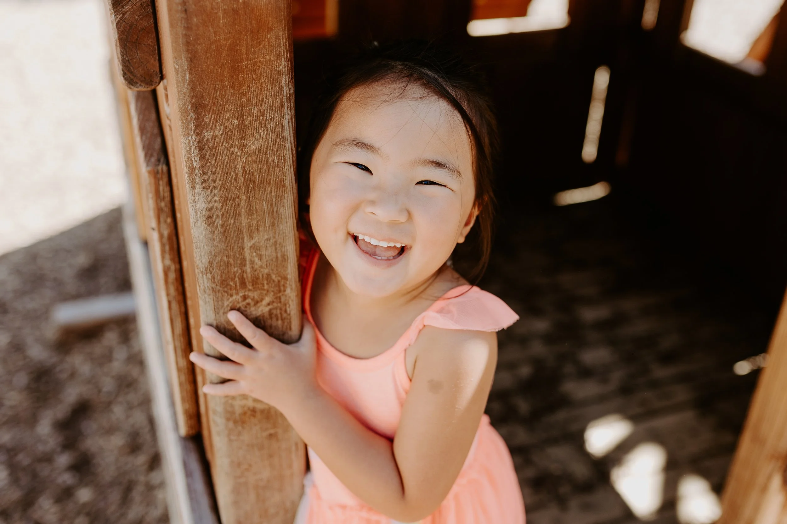 Little girl holds onto a wooden beam at a playground