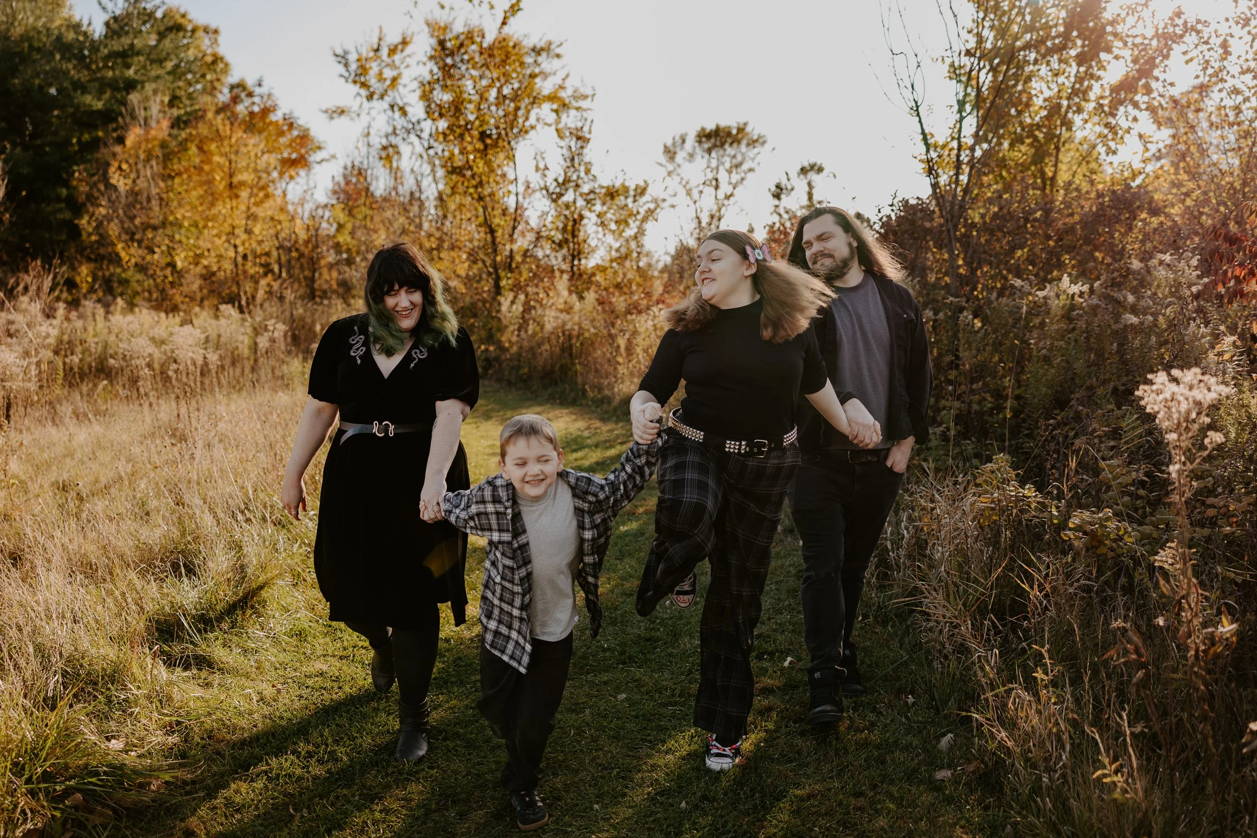 A family of four skips through tall grass at golden hour
