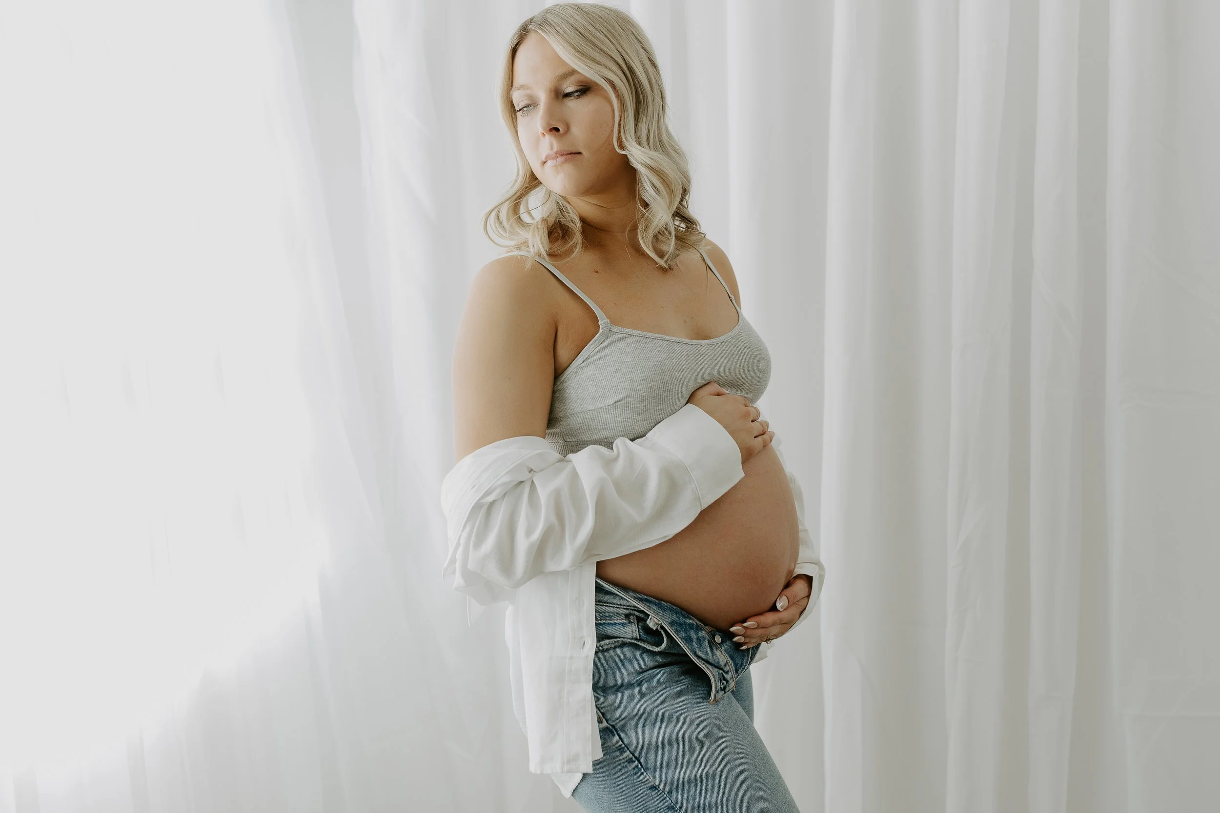 An expecting mother holds her belly in front of a white backdrop