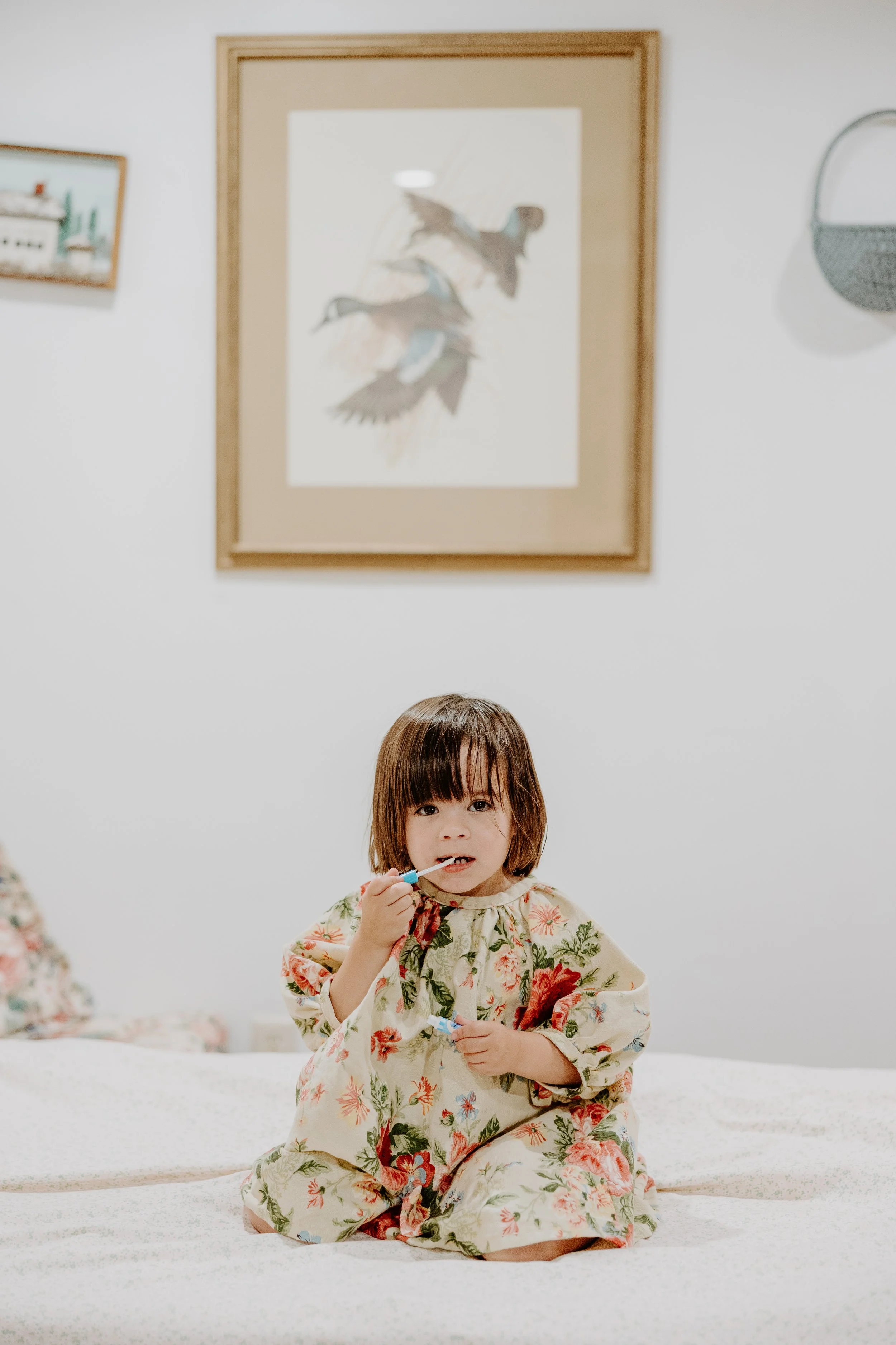 Little girl sits on her bed and puts on way too much lipgloss