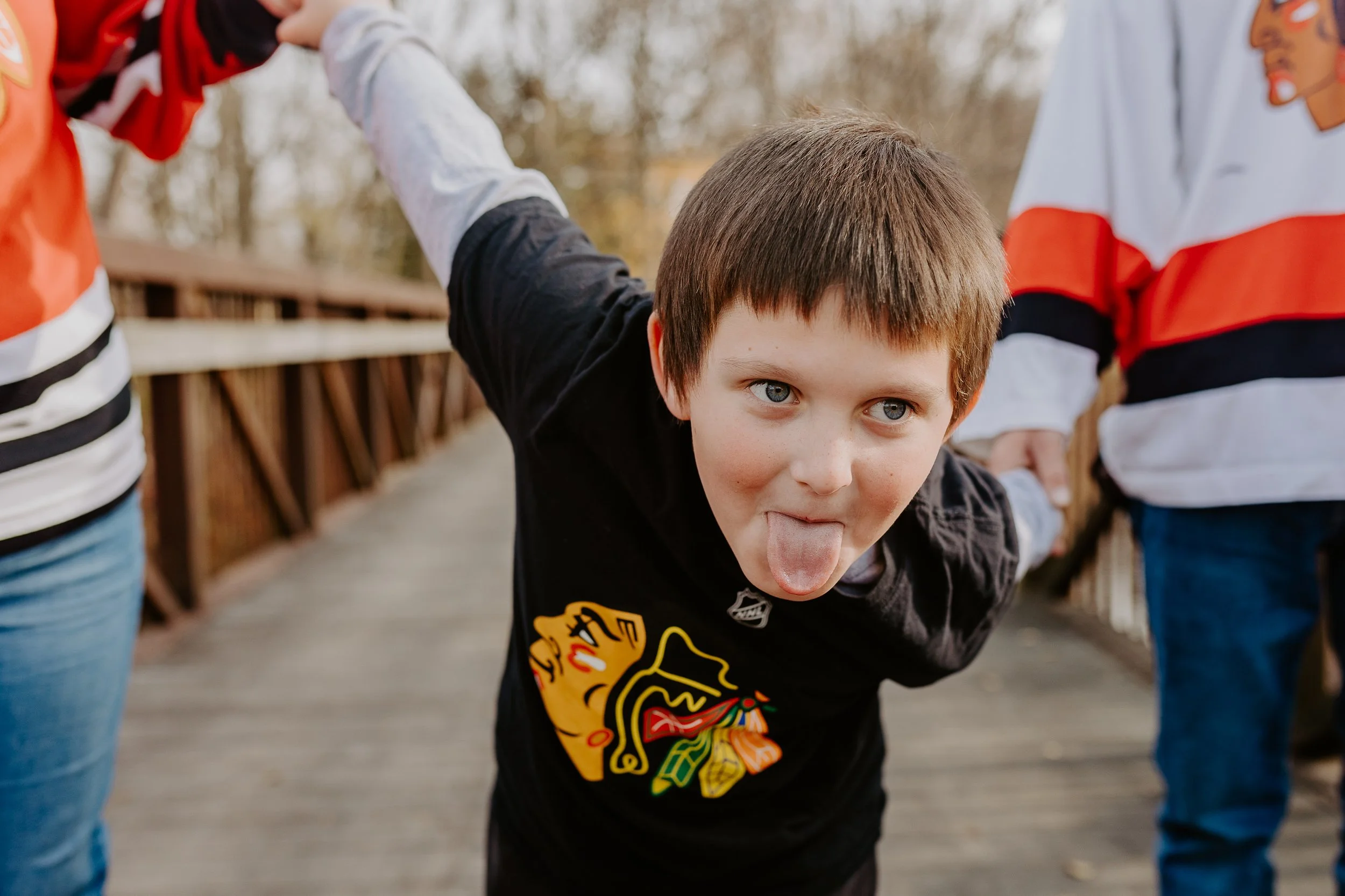 A little boy pulls his mom and dad behind him and playfully sticks his tongue out