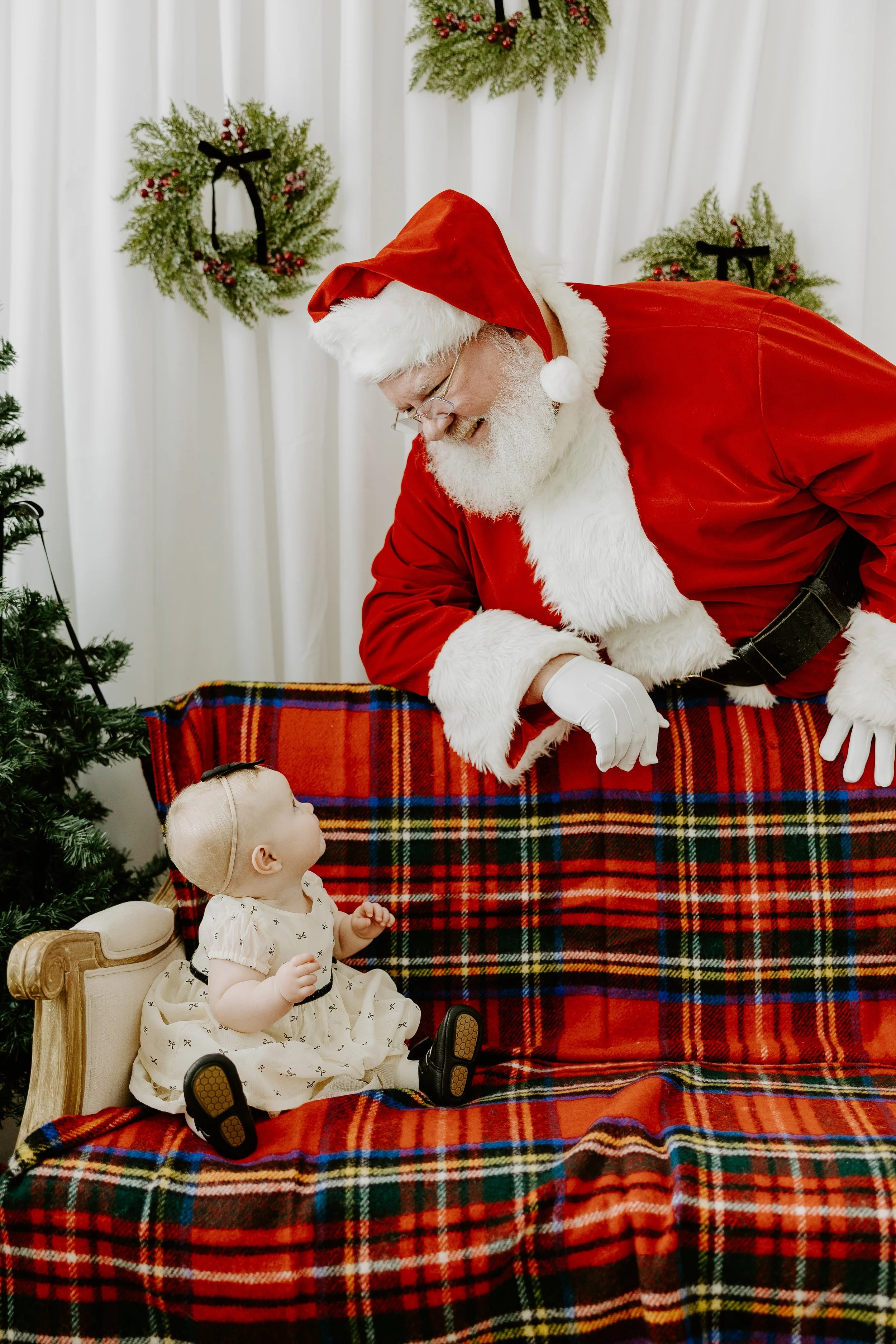 A baby sitting on a couch lookin up at Santa