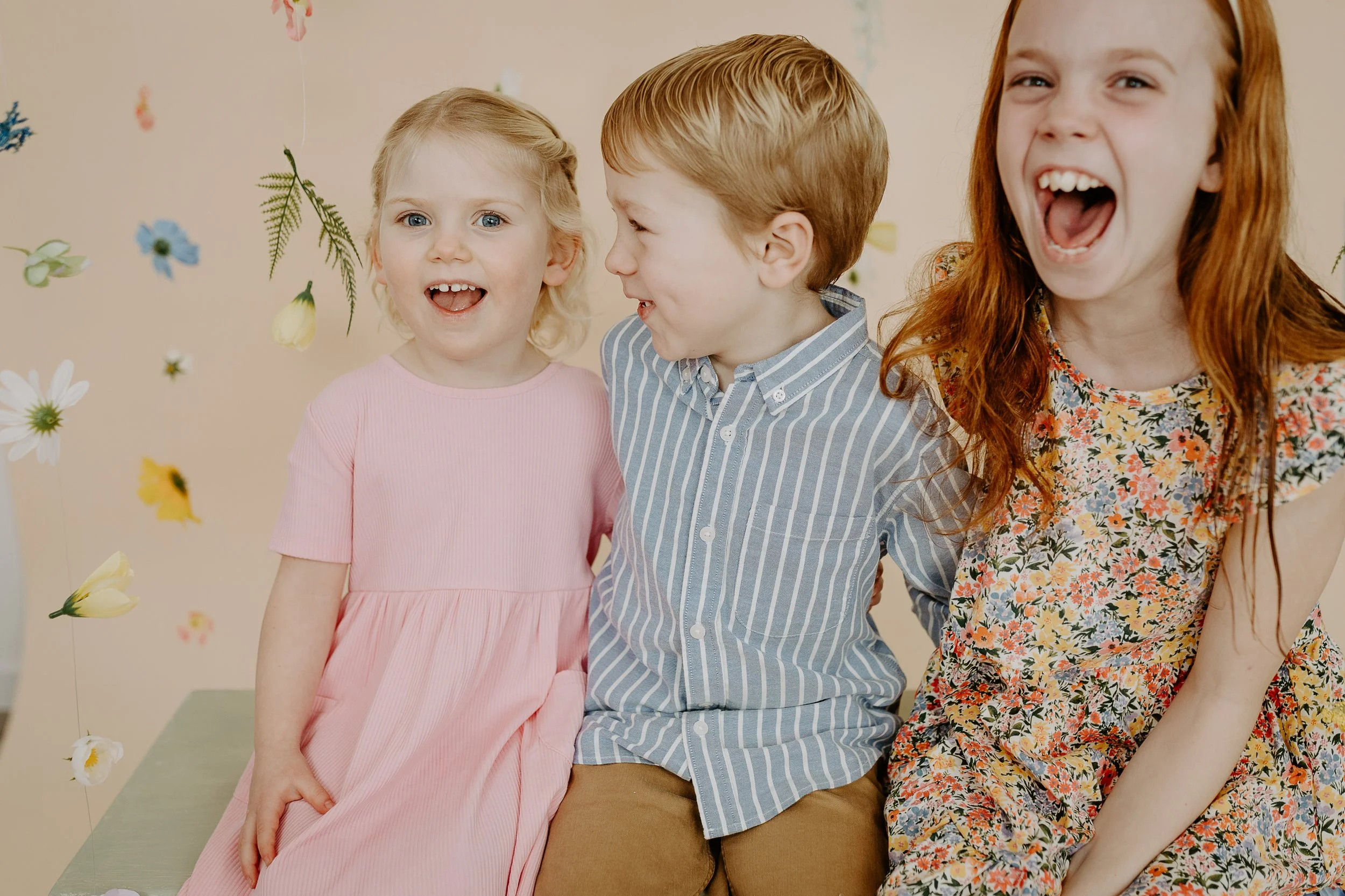 three kids on a bench laughing in front of floating flowers