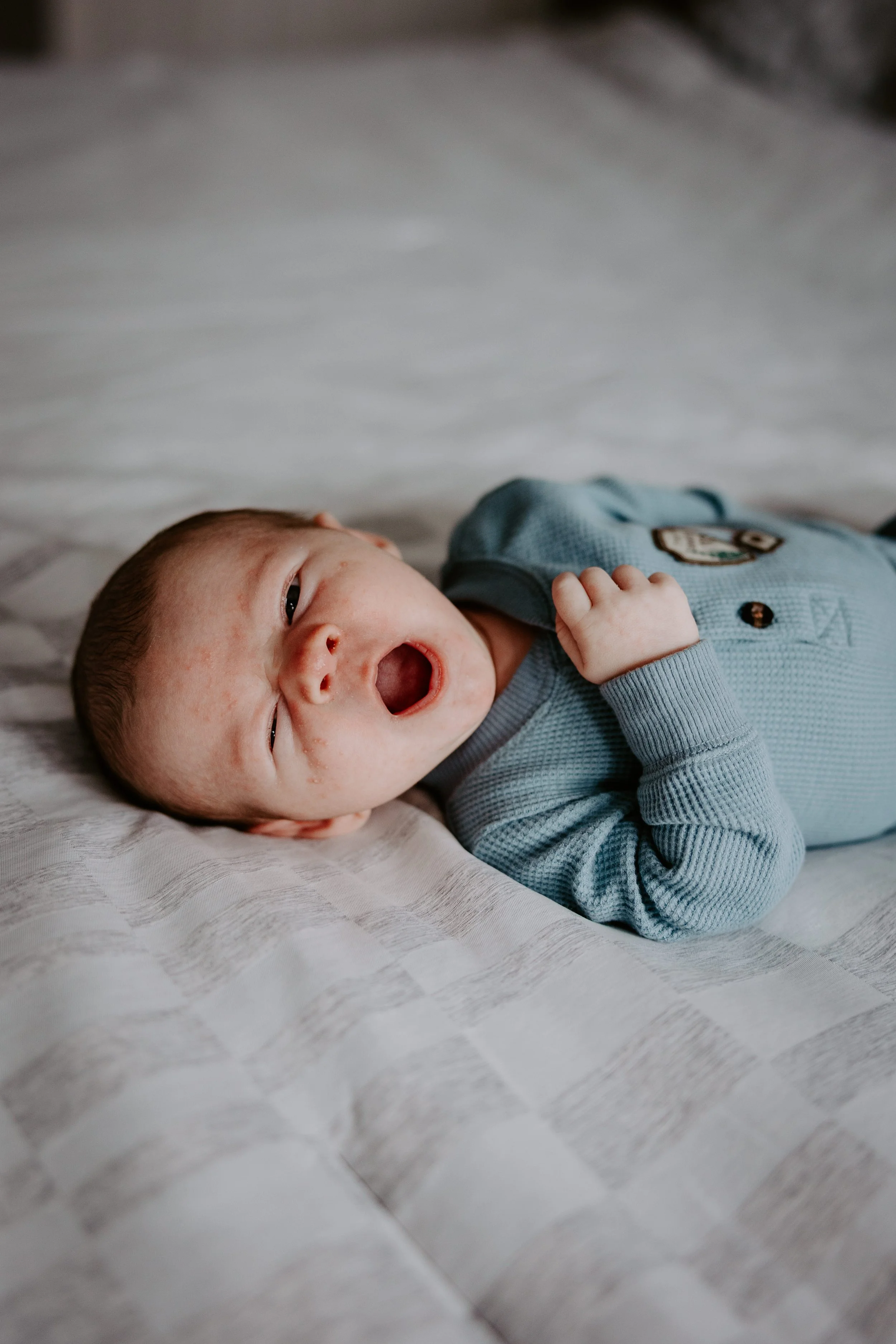 A newborn in a blue pj set yawns