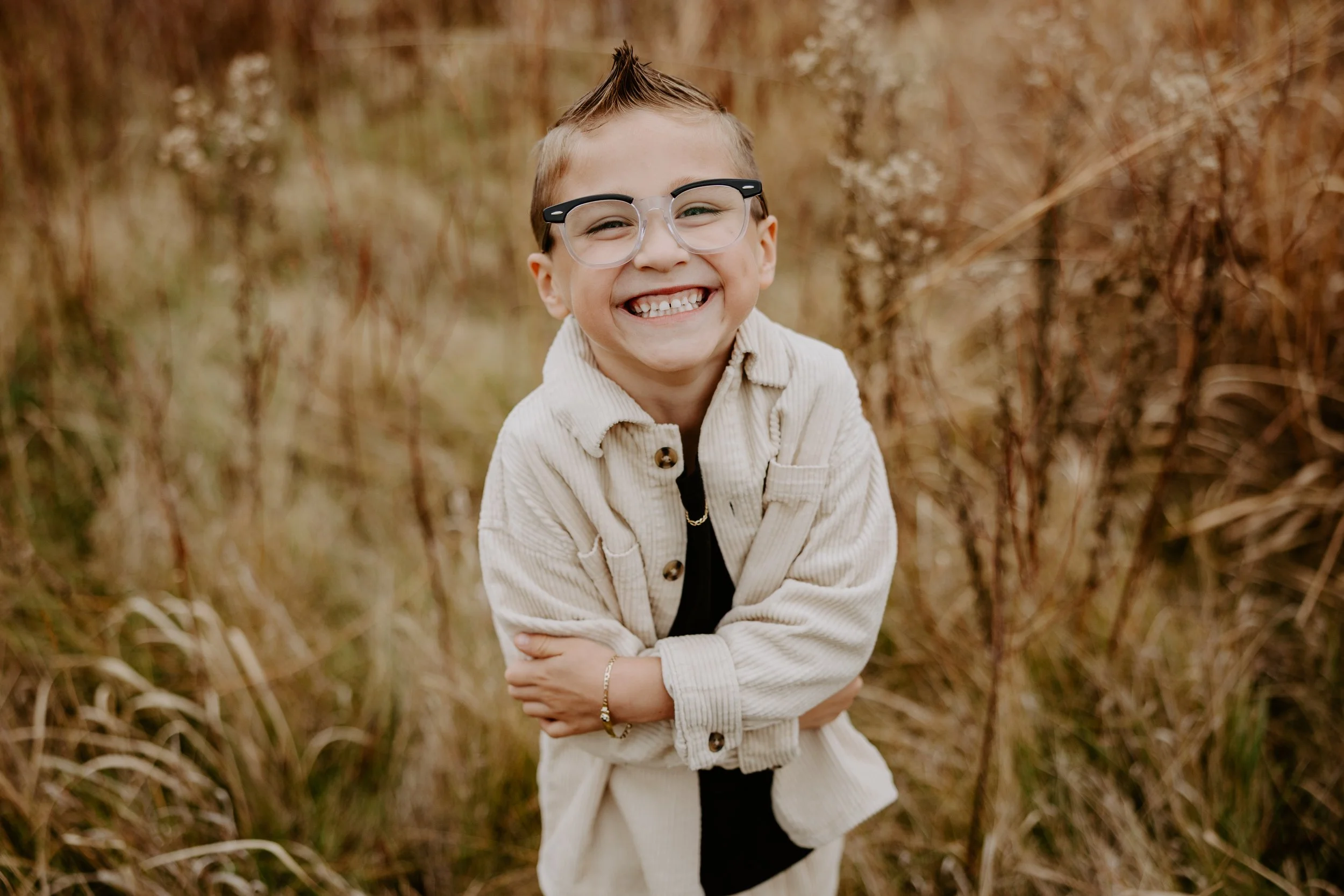 Little boy with glasses smiles at the camera in a field of wild grass