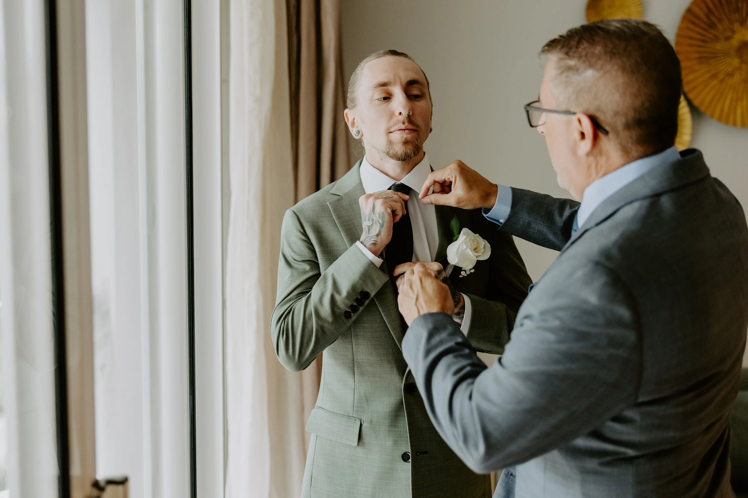 A dad helps his son with his tie before his wedding