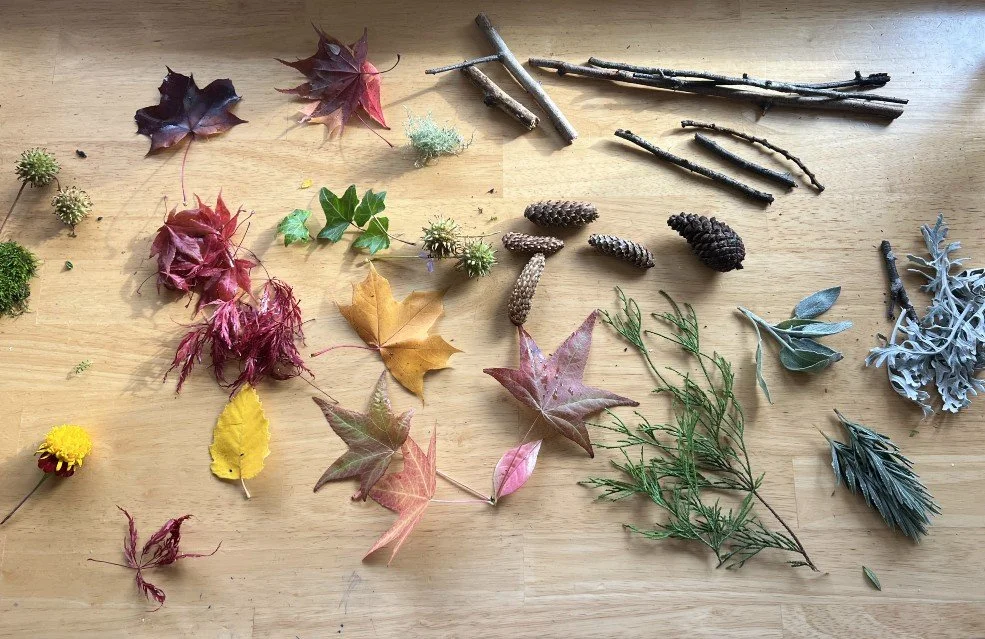 A collection of autumn leaves, pinecones, twigs, and other natural objects spread out on a wooden surface.