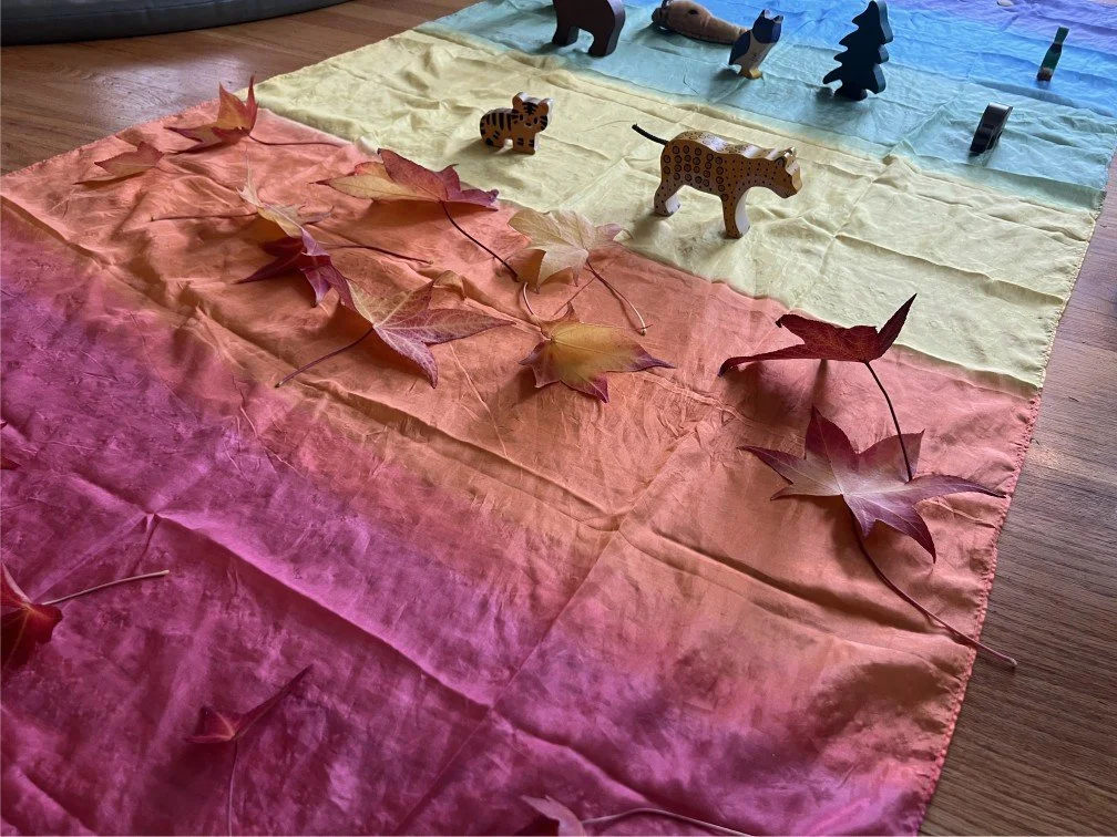 Colorful fabric with autumn leaves and wooden animal figurines on top, depicting a scenic landscape.