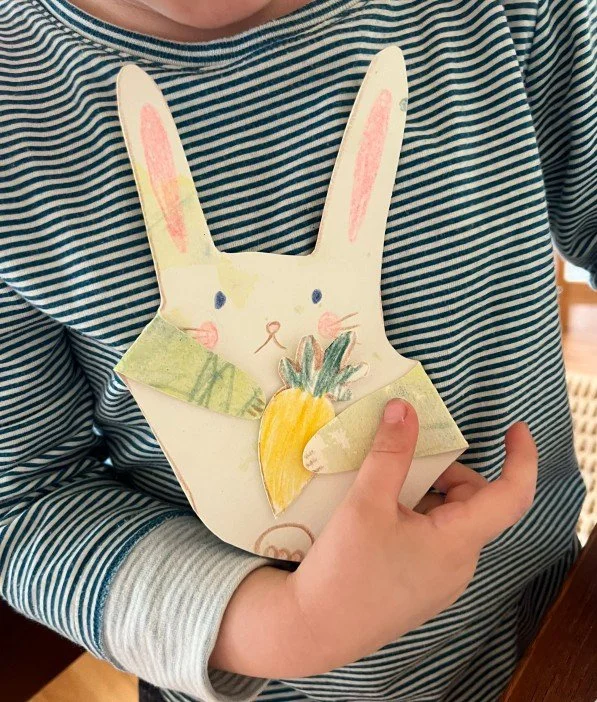 Child in a striped shirt holding a handmade paper cutout of a rabbit with a carrot.