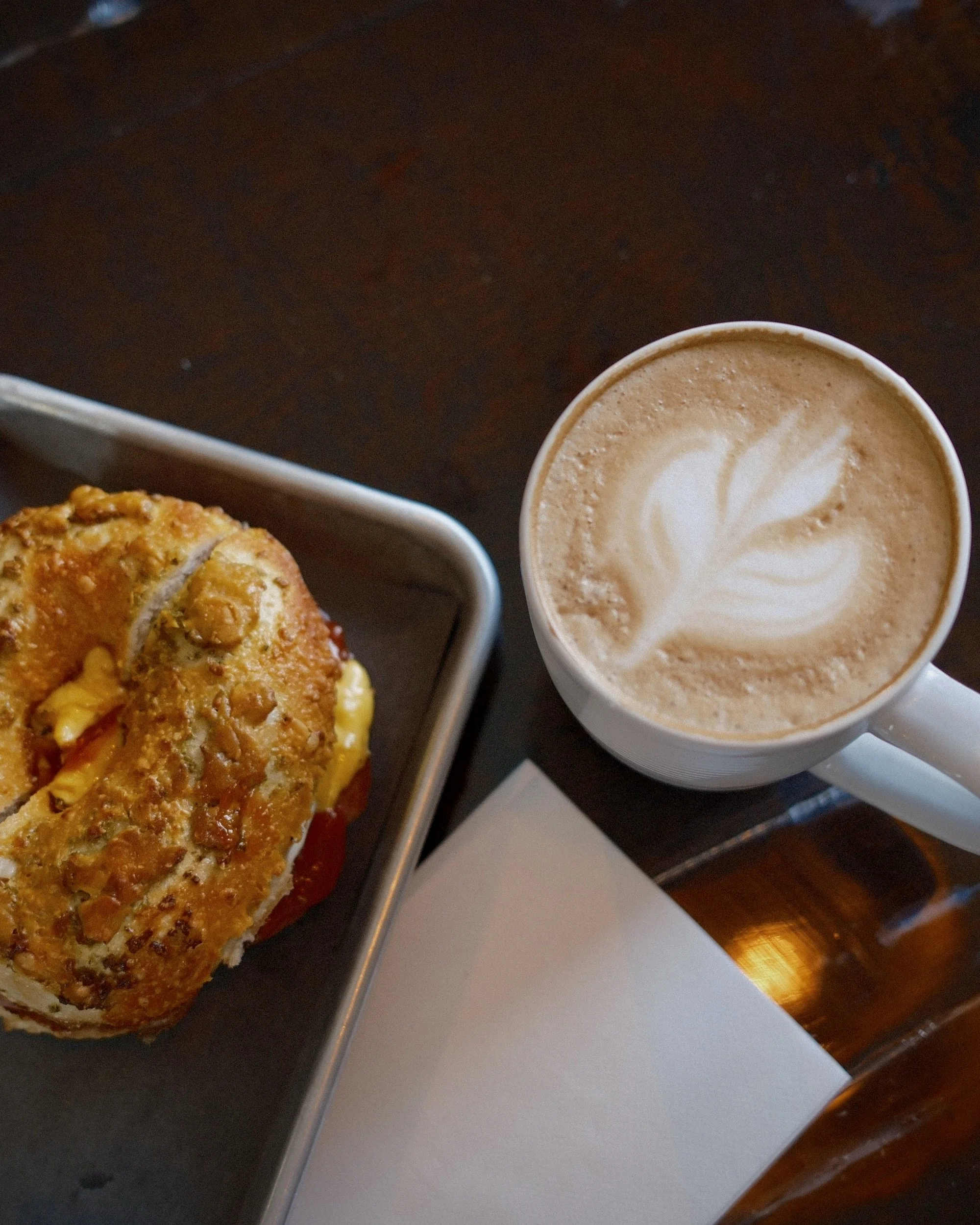 A latte with latte art in a white mug next to a cheese omelette on a metal tray on a dark wooden table.