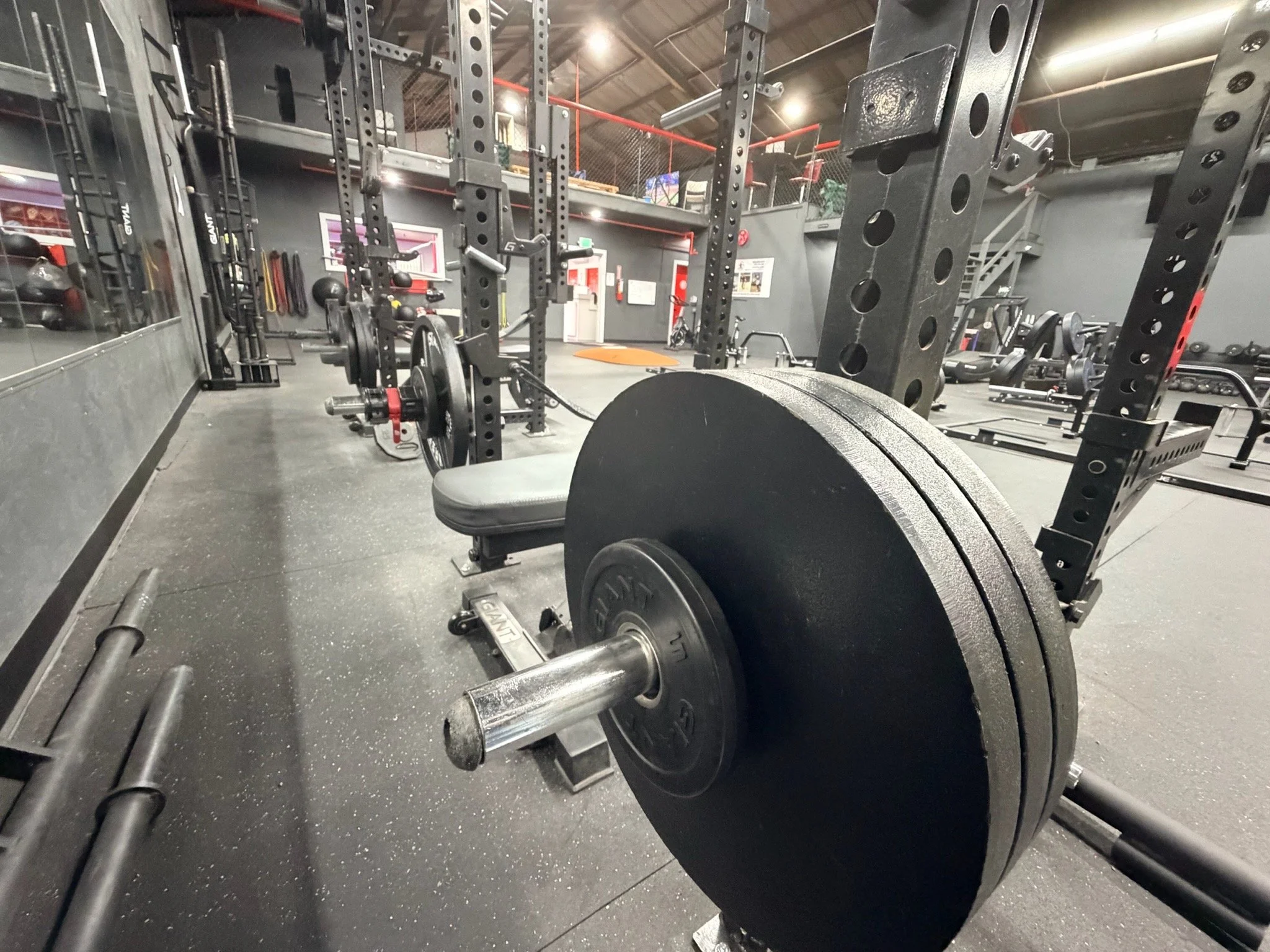 Gym weightlifting area with a loaded barbell on a squat rack, surrounded by weight plates, benches, and resistance bands, in a well-lit fitness center.