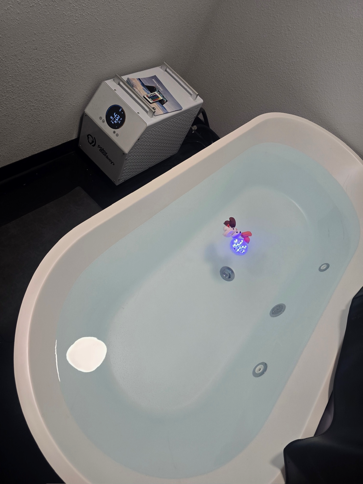 A bathtub filled with water with a small animated Christmas ornament floating inside. A neighborhood scene is reflected in the water. A portable heater is positioned near the bathtub.