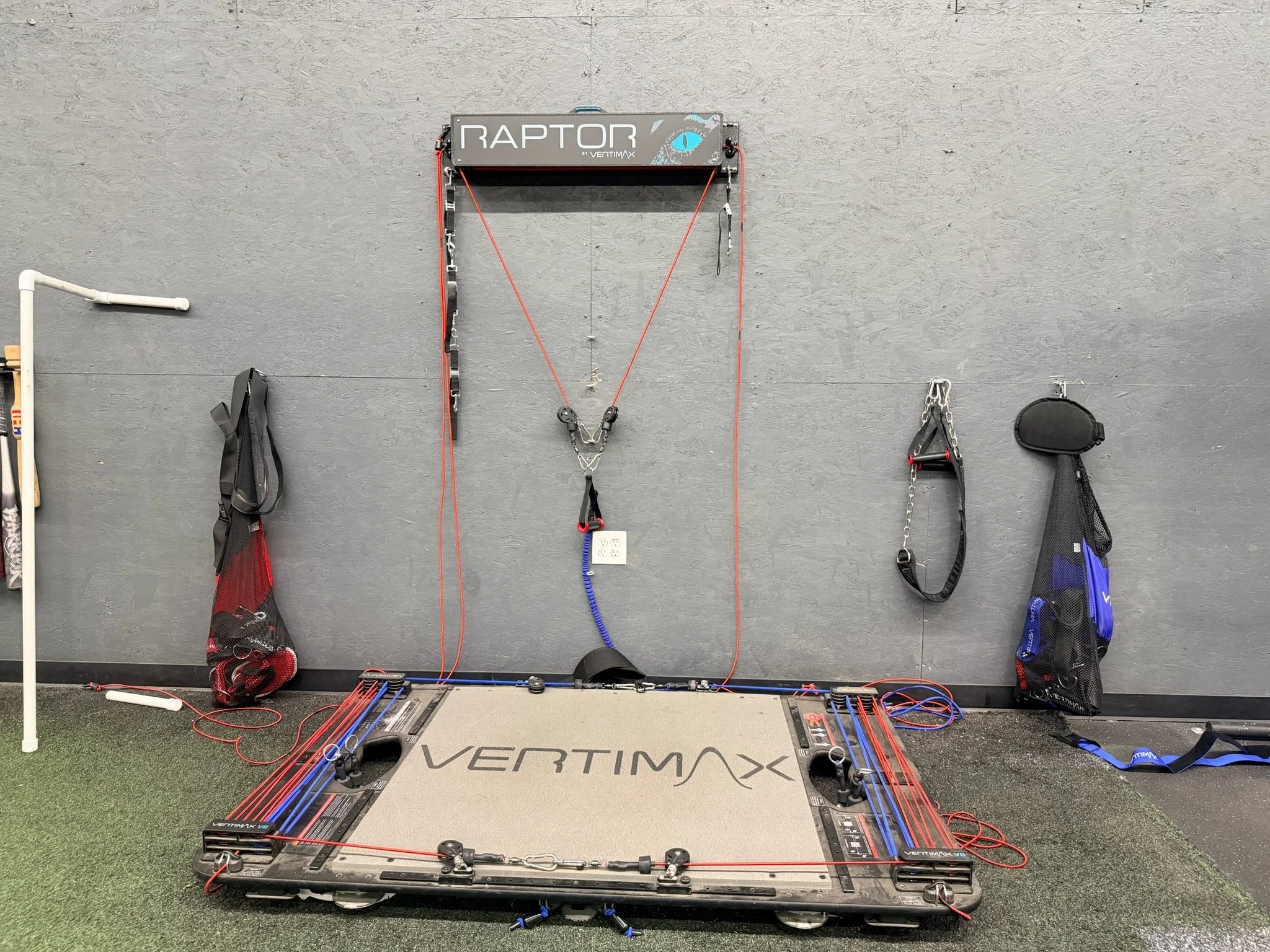 Indoor training setup with a Vertimax Raptor resistance training platform, resistance cords, and various fitness accessories hanging on the wall.