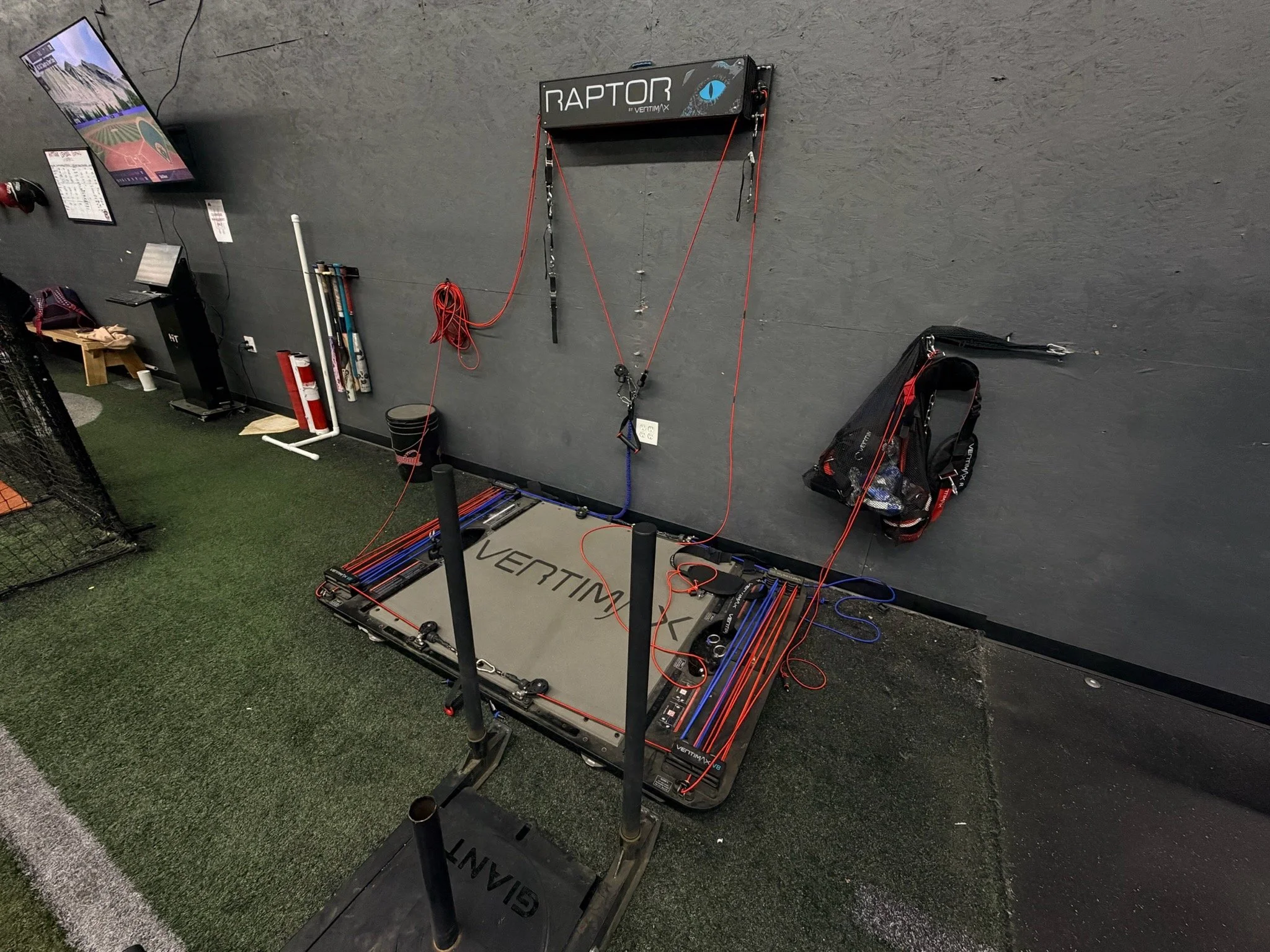 Indoor training setup for sports simulation, featuring a Raptor wall with resistance bands and a VERT CORE vertimax training platform on artificial turf.