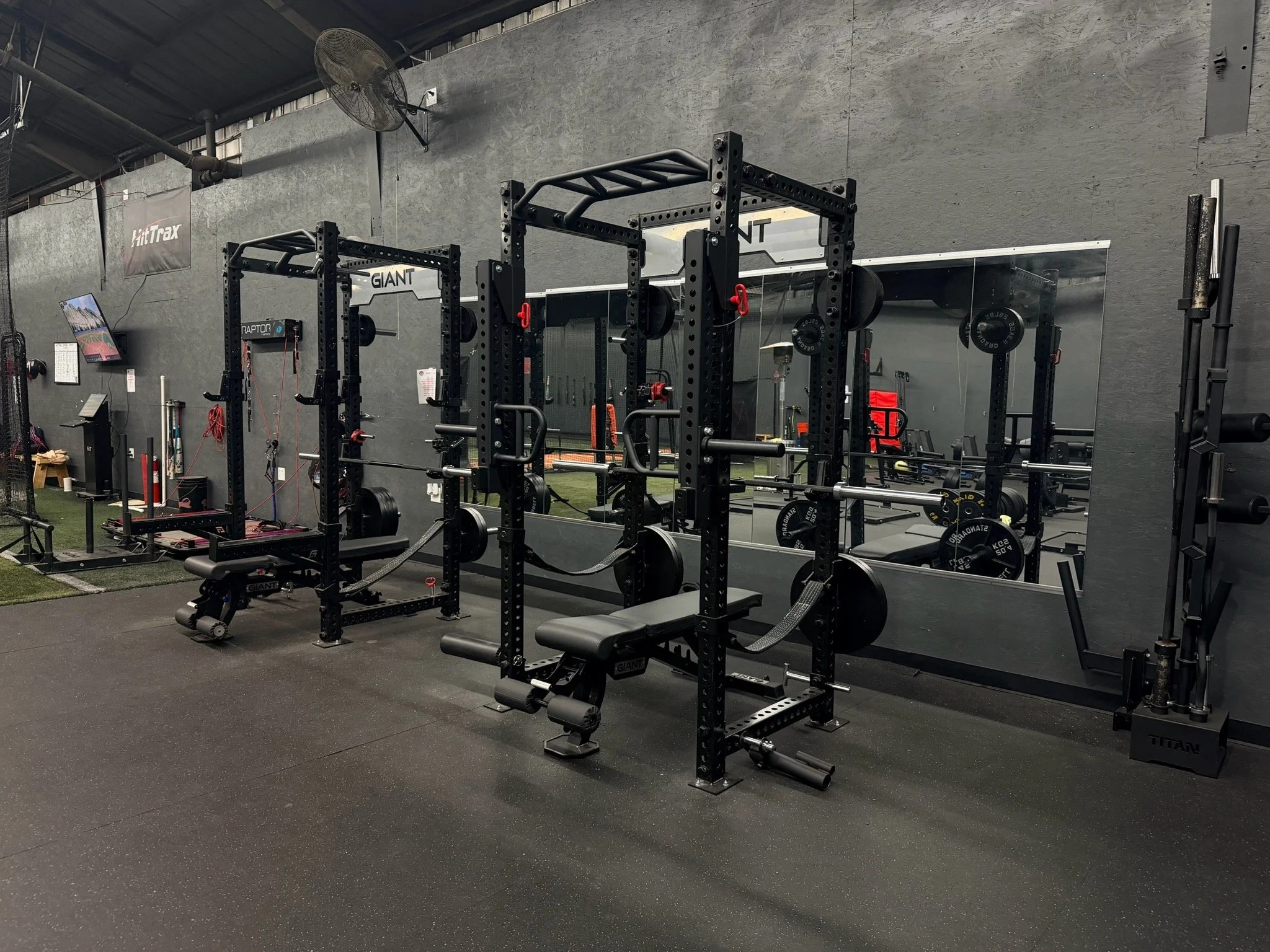 Glen workout gym with black power racks, weight plates, benches, and a large mirror on the wall, with gym equipment visible in the background.