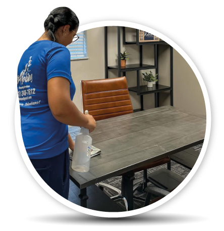 Person cleaning a conference room table with a spray bottle in an office setting.