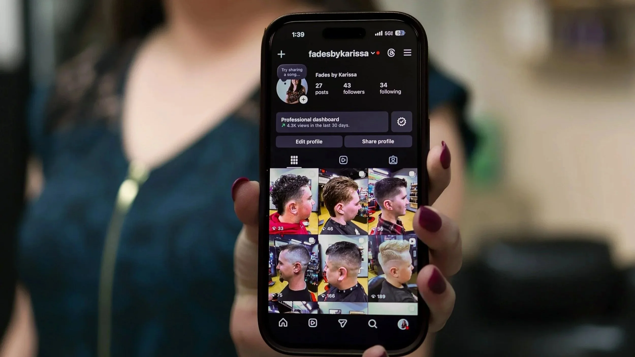 A person holding a smartphone displaying an Instagram profile of a user named fadesbykarissa, showing profile description and multiple photos of different hairstyles of a young men.