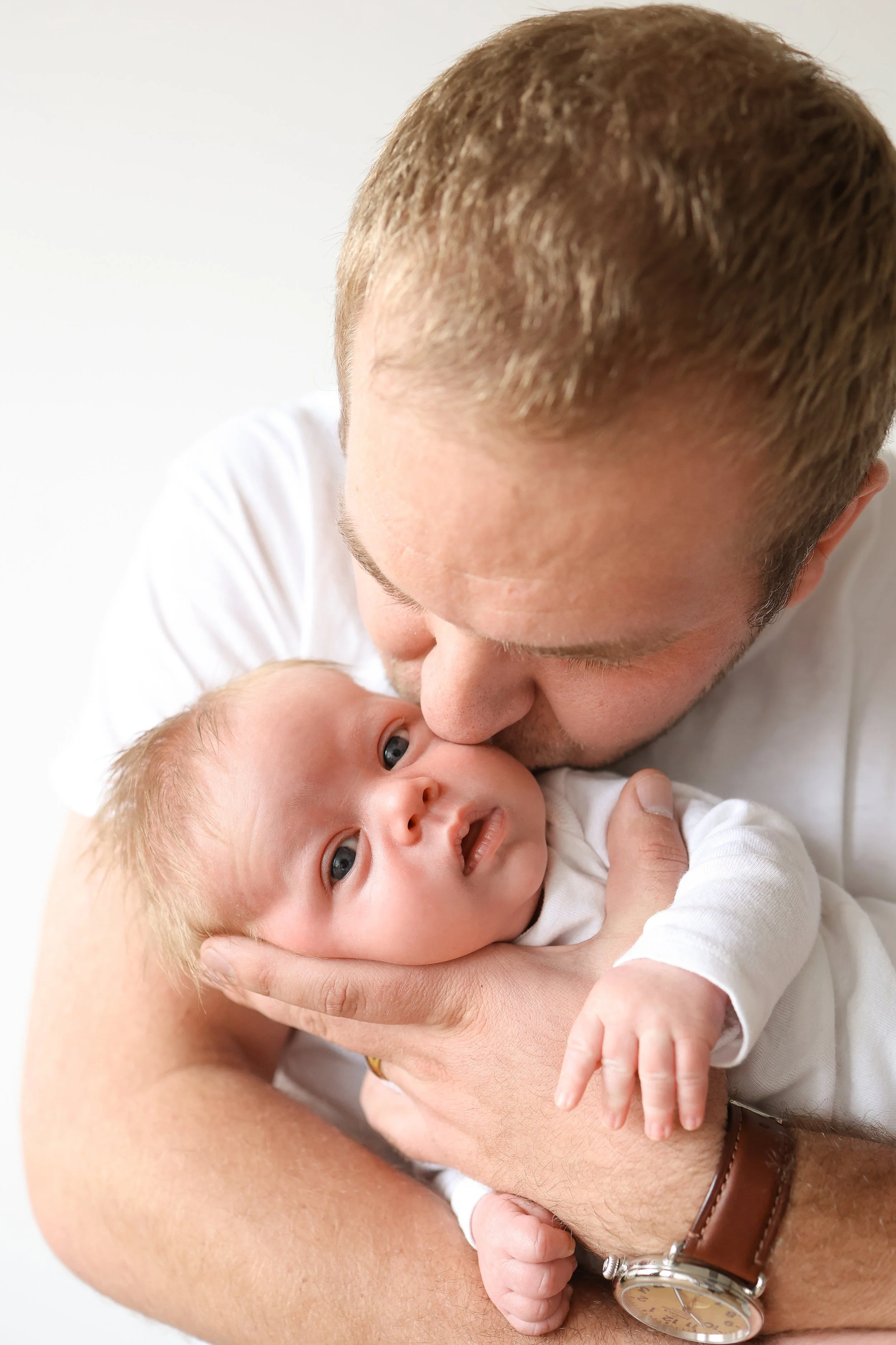 A man with light brown hair holding and gently kissing a baby with blond hair and blue eyes.