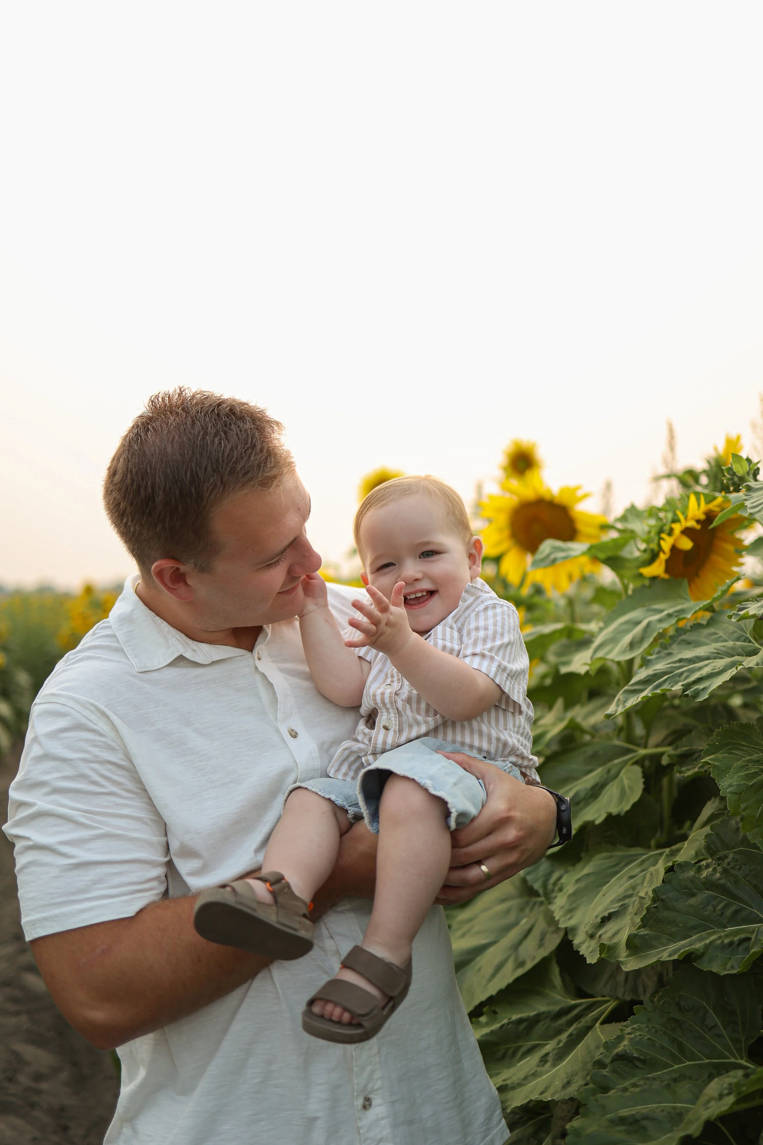 A man holding a smiling child in a sunflower field
