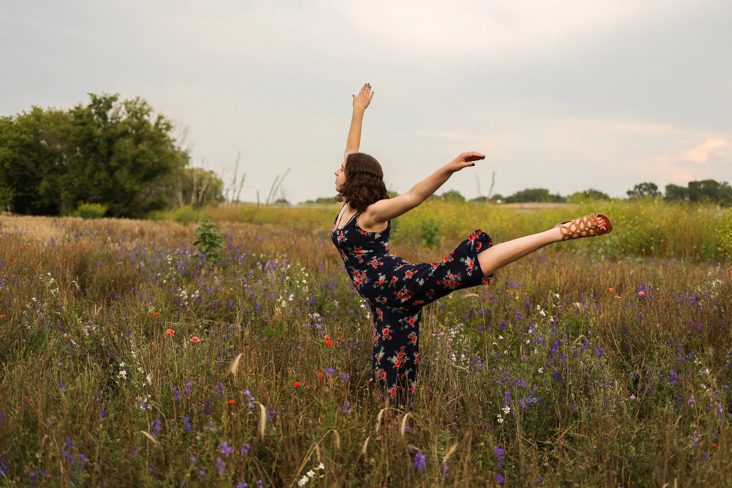A woman in a floral dress practicing ballet in a field of wildflowers.