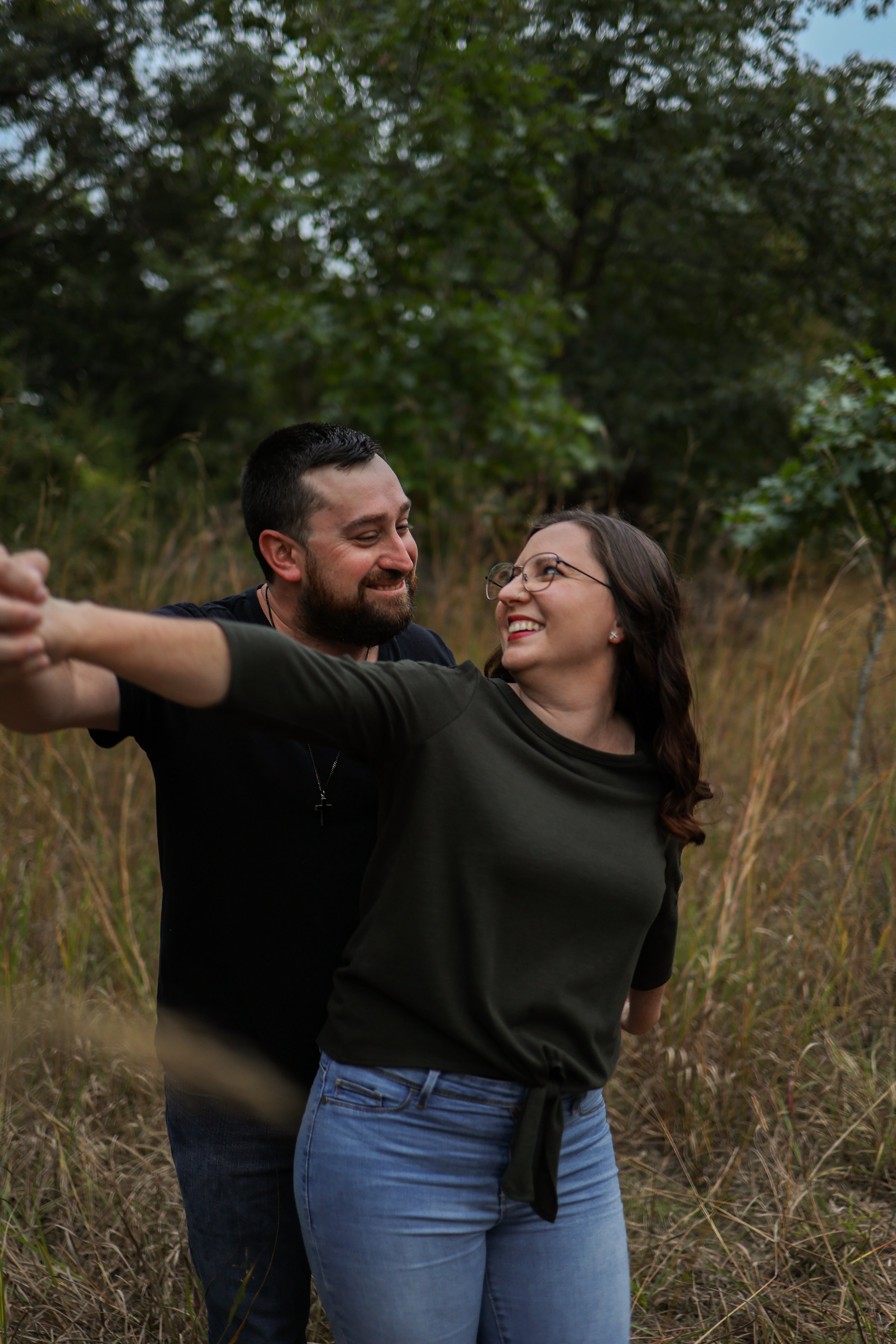 A couple dancing outdoors in a grassy field with trees in the background.