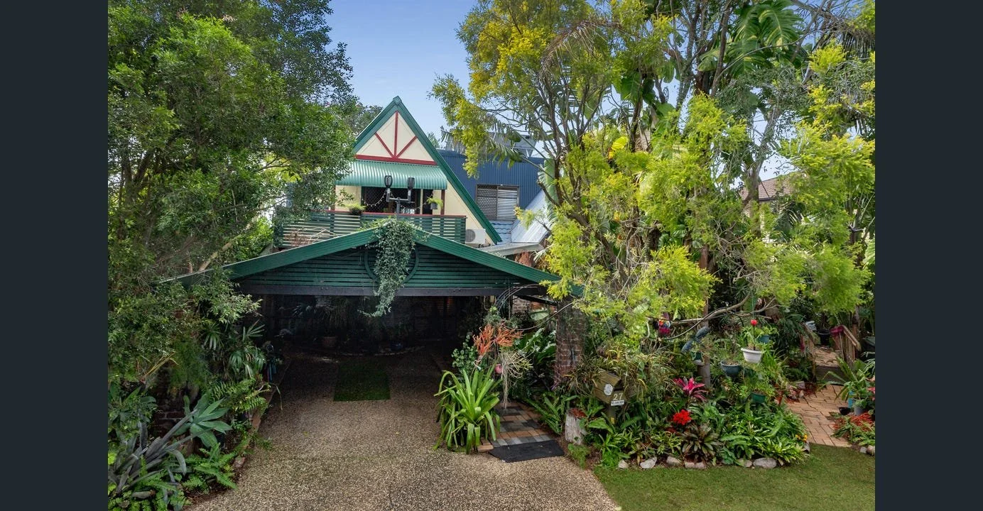A house with a green roof and trim surrounded by lush greenery and colorful plants.