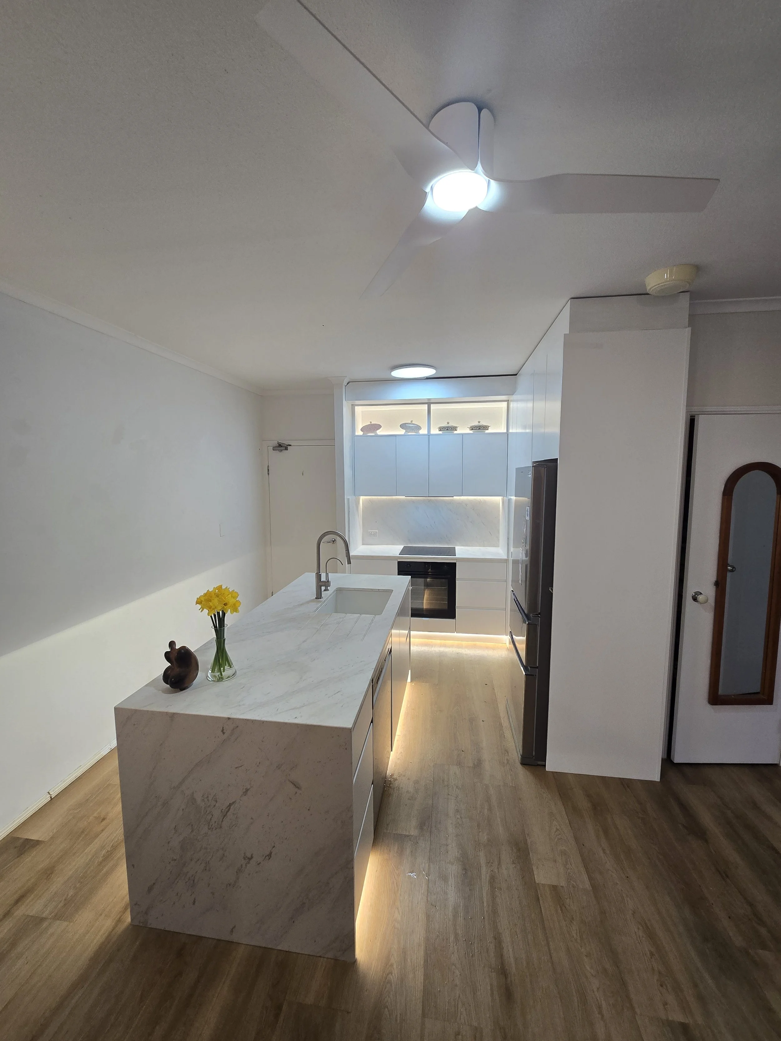 Modern kitchen with marble island, white cabinetry, stainless steel appliances, a sink, and a vase of yellow flowers on the island.