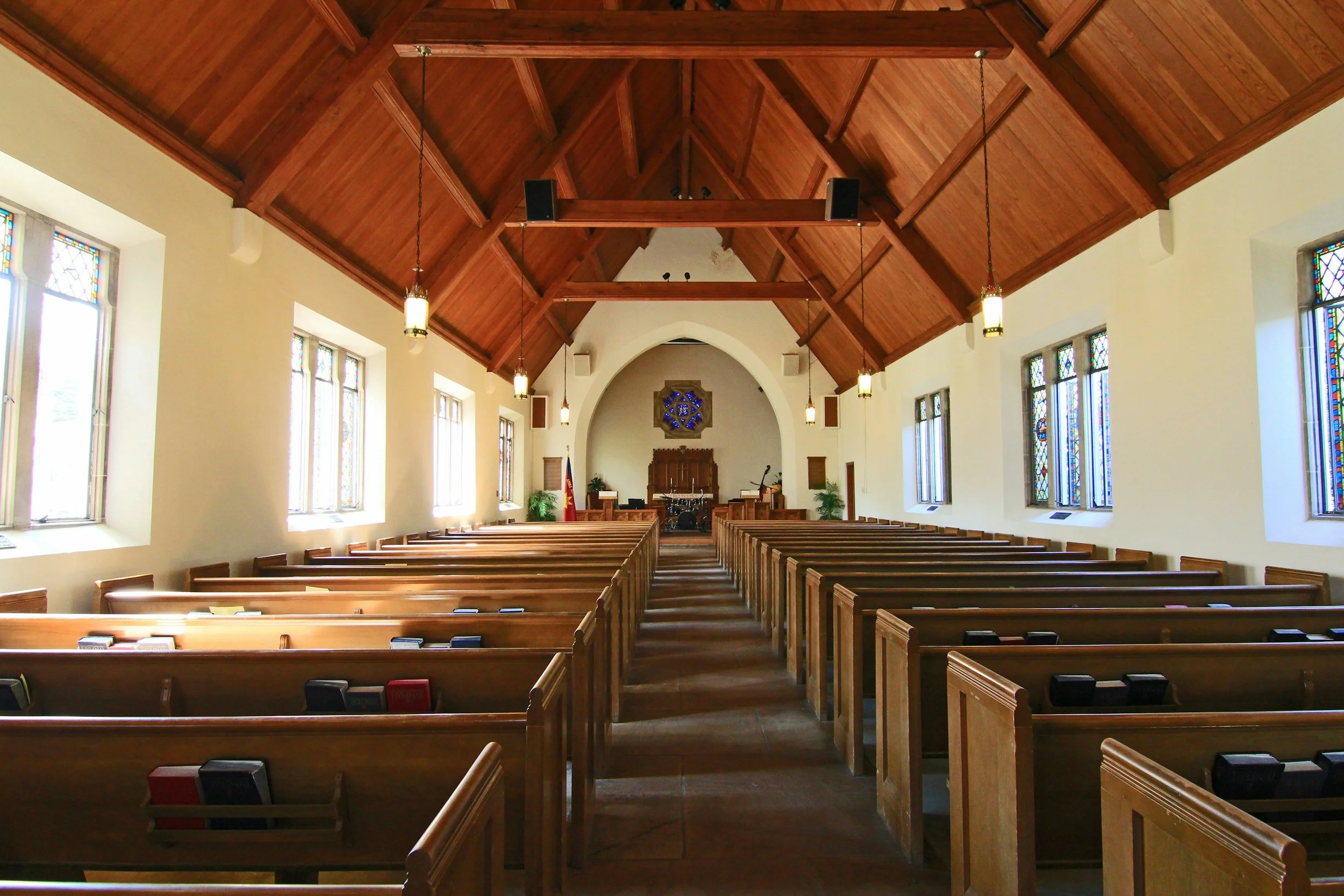 Interior of a church with wooden pews facing the altar, stained glass windows on the sides, and a vaulted wooden ceiling.