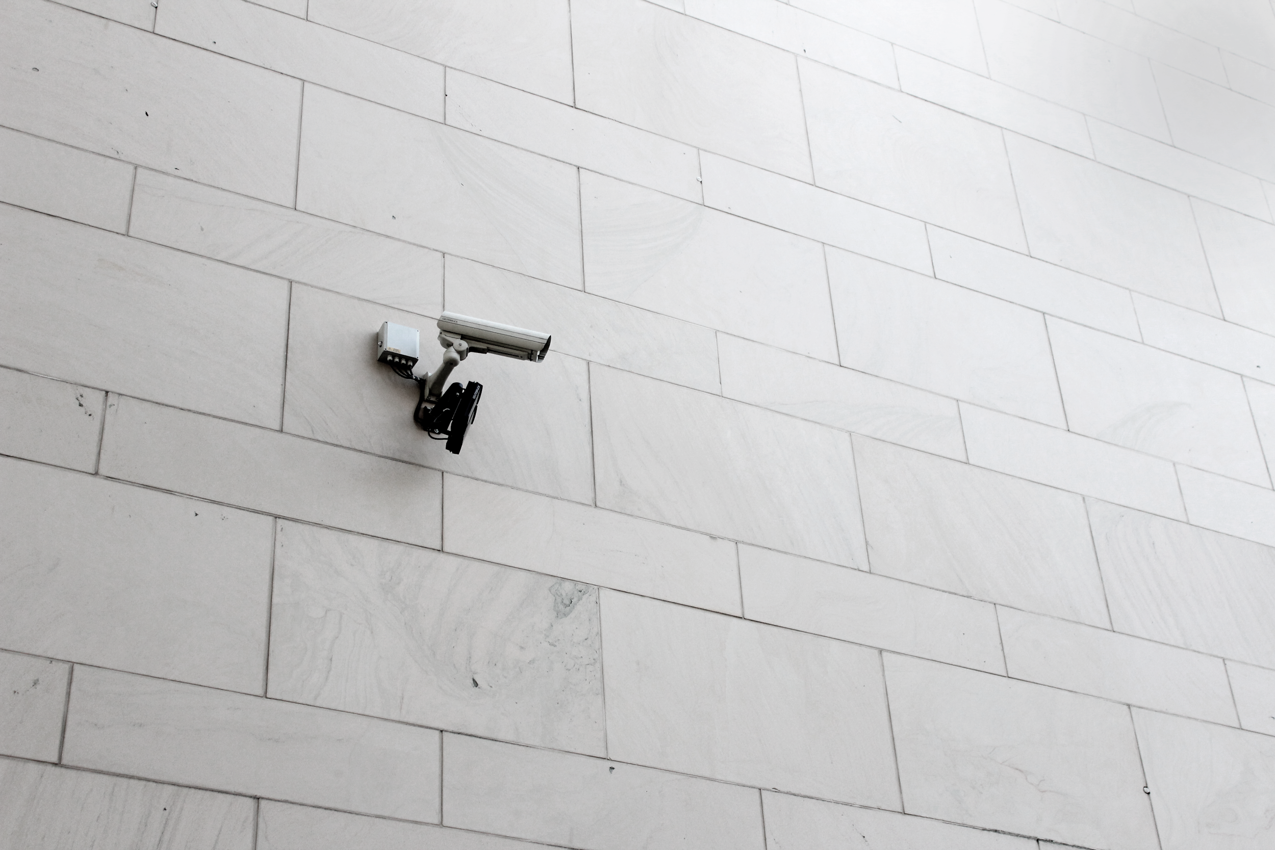A security camera mounted on a white tiled wall.