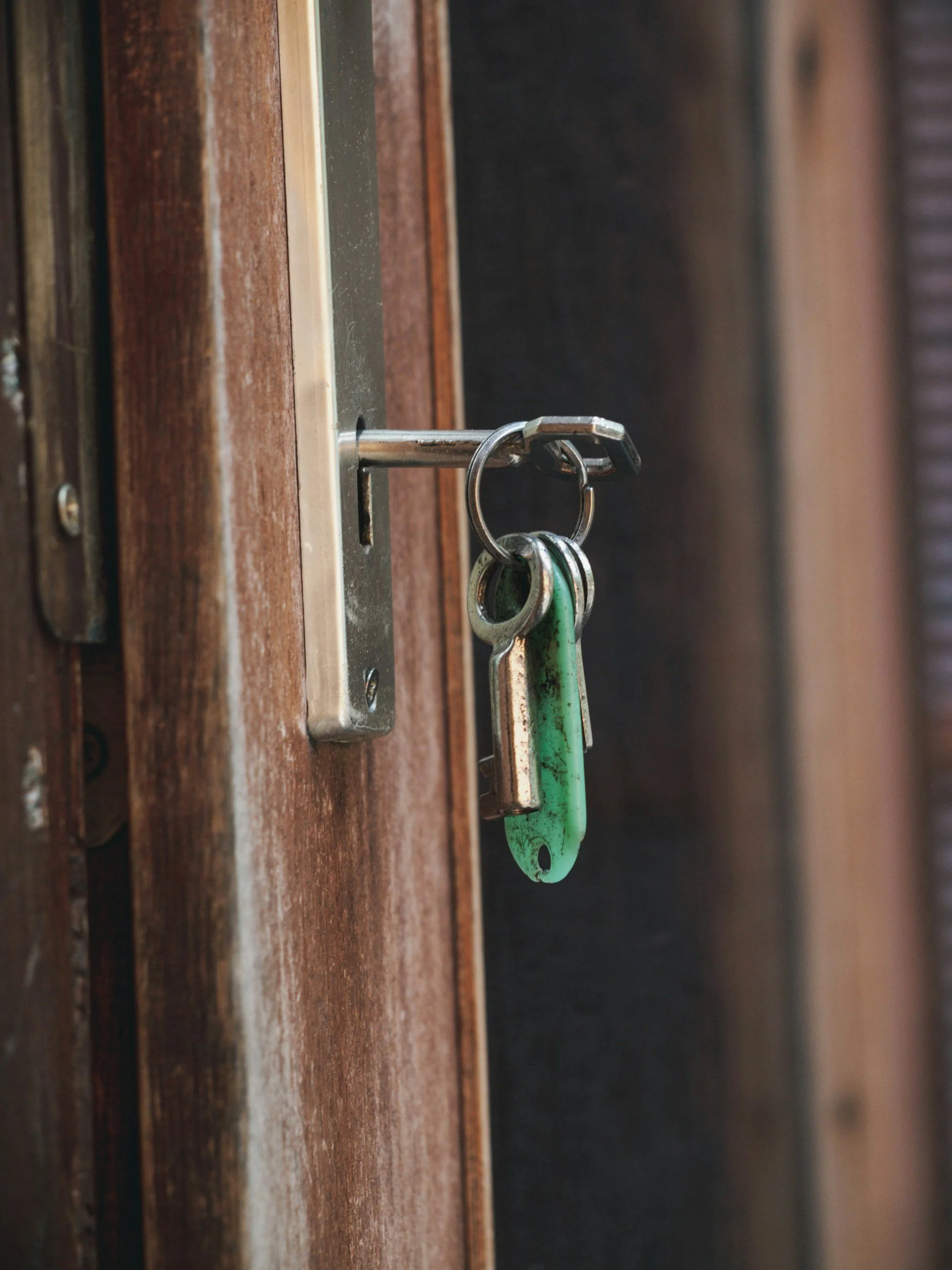 A close-up of a door lock with a key chain hanging from the lock, attached to a wooden door.