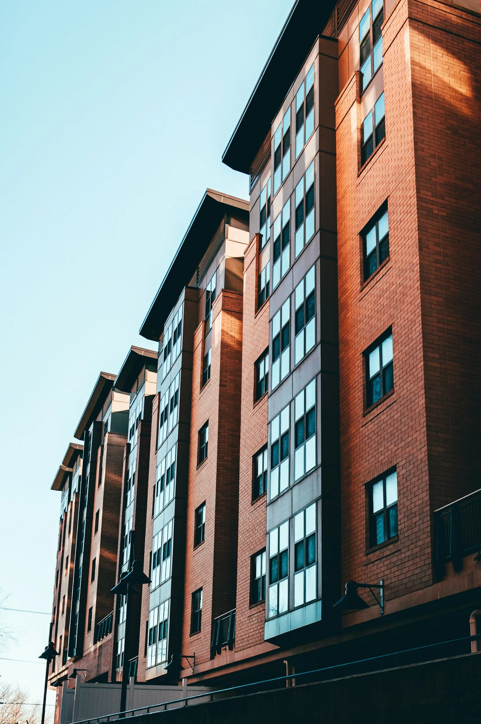 Tall modern apartment building with brick facade and large windows, set against a clear blue sky.