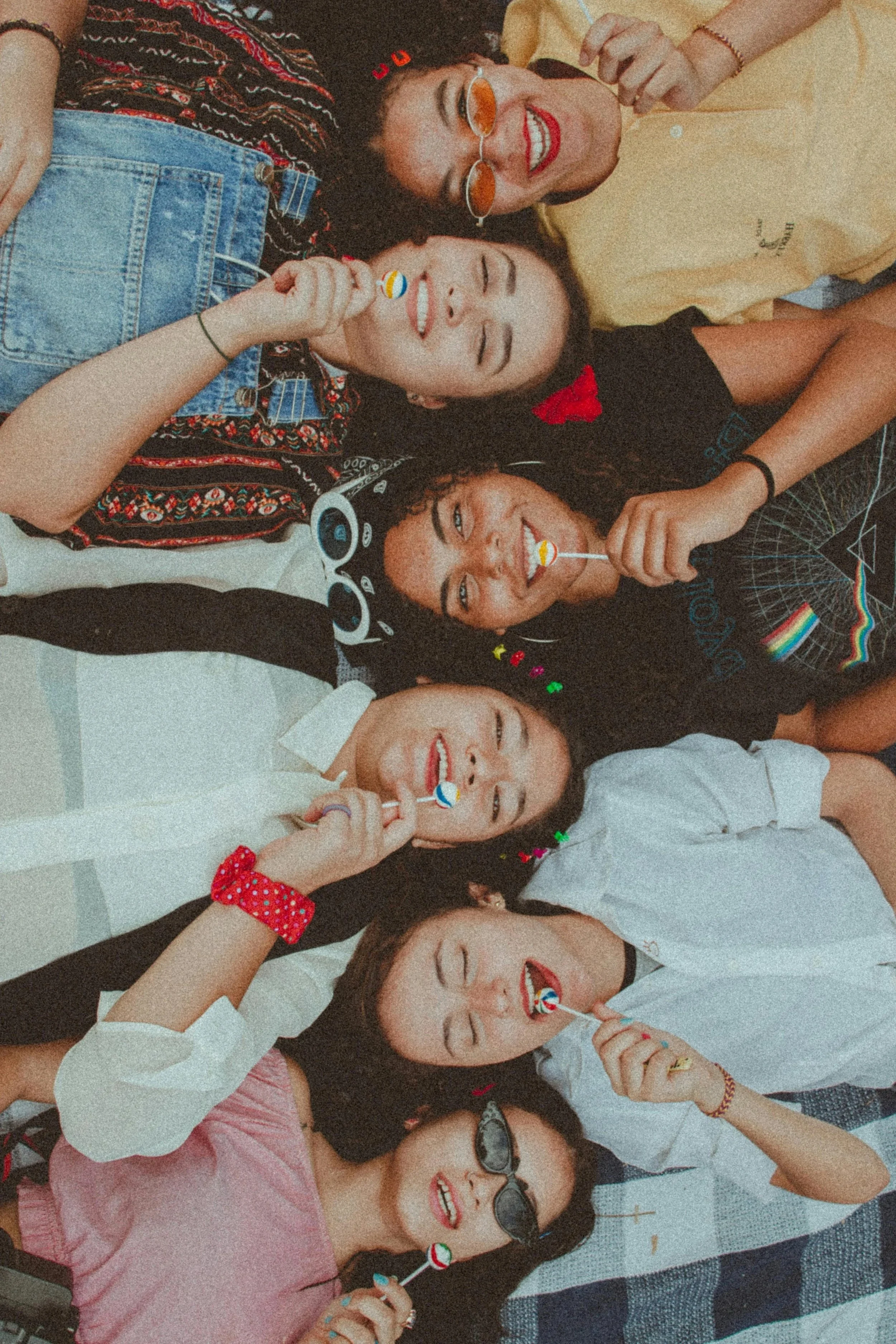 Group of diverse young women lying on the floor, smiling, wearing casual clothes, holding colorful lollipops, celebrating and having fun.