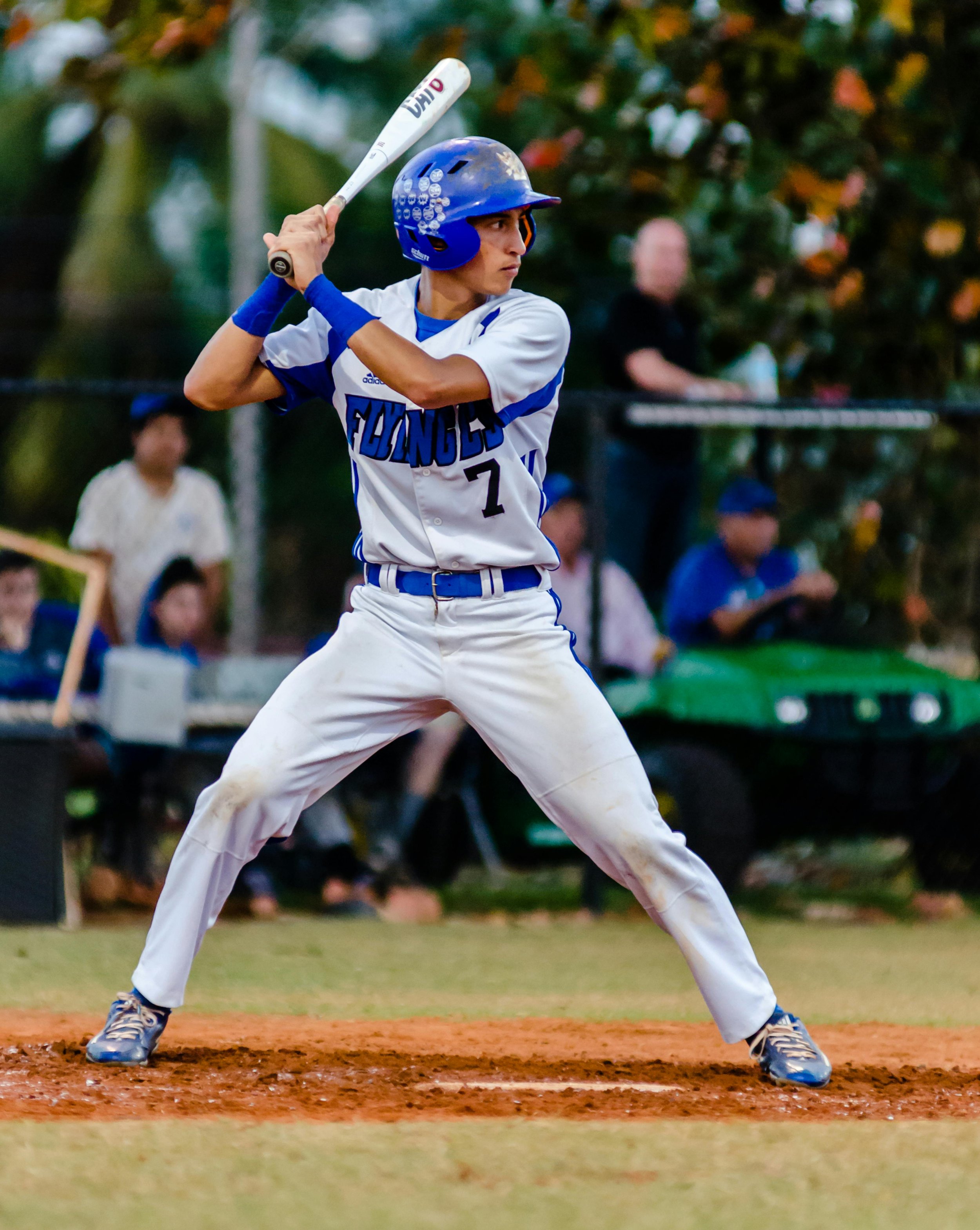 A young baseball player wearing a white and blue uniform and helmet, holding a bat in a batting stance during a game.