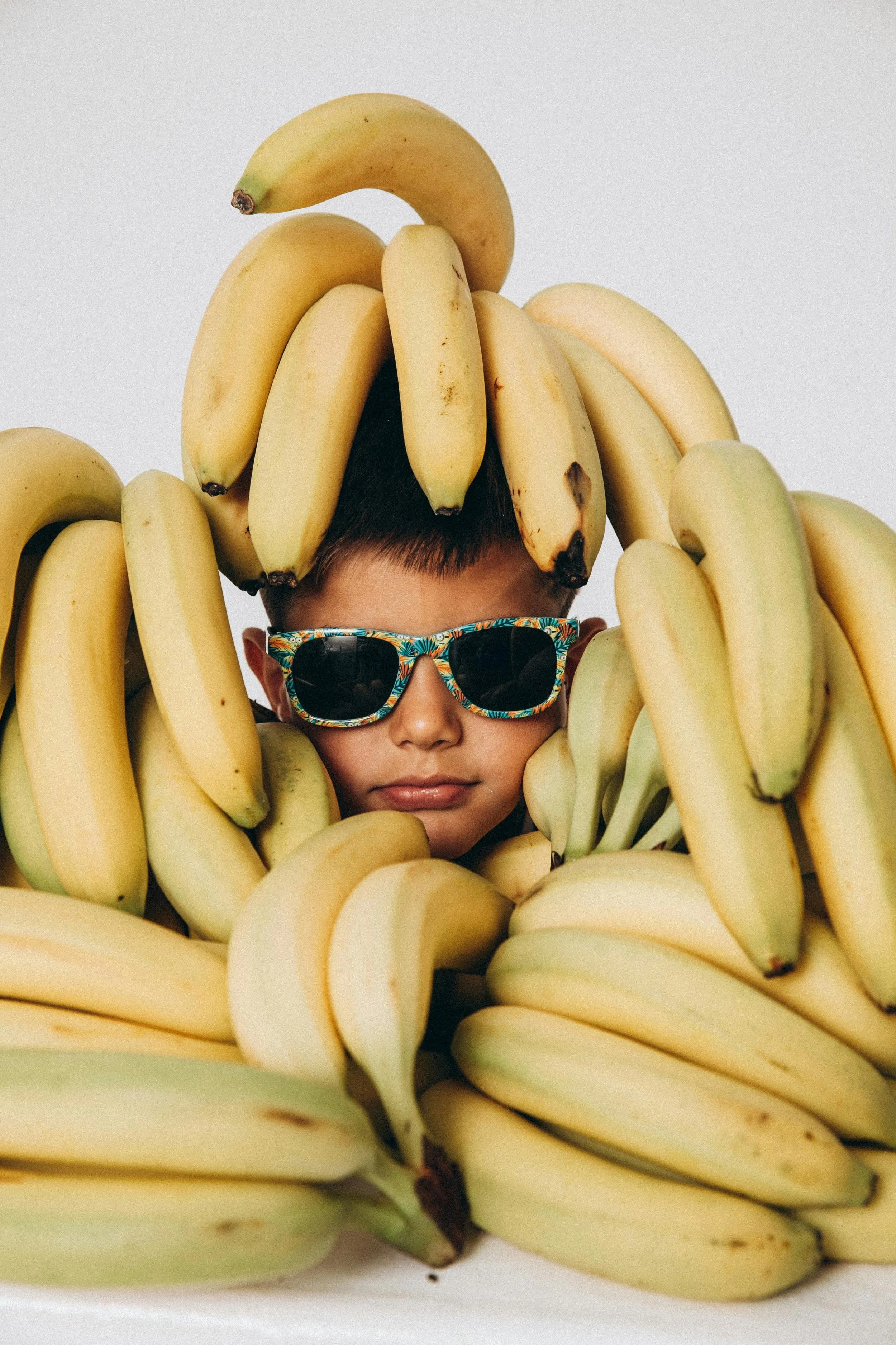 ADHD San Mateo Person wearing sunglasses surrounded by bananas, with some bananas on their head.