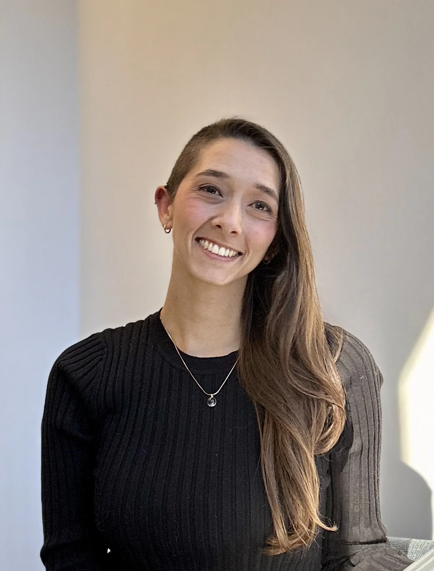 Dr. Griest, a Bay Area Psychologist, female, with long brown hair on the left side of her head, sitting and smiling in front of an off-white background