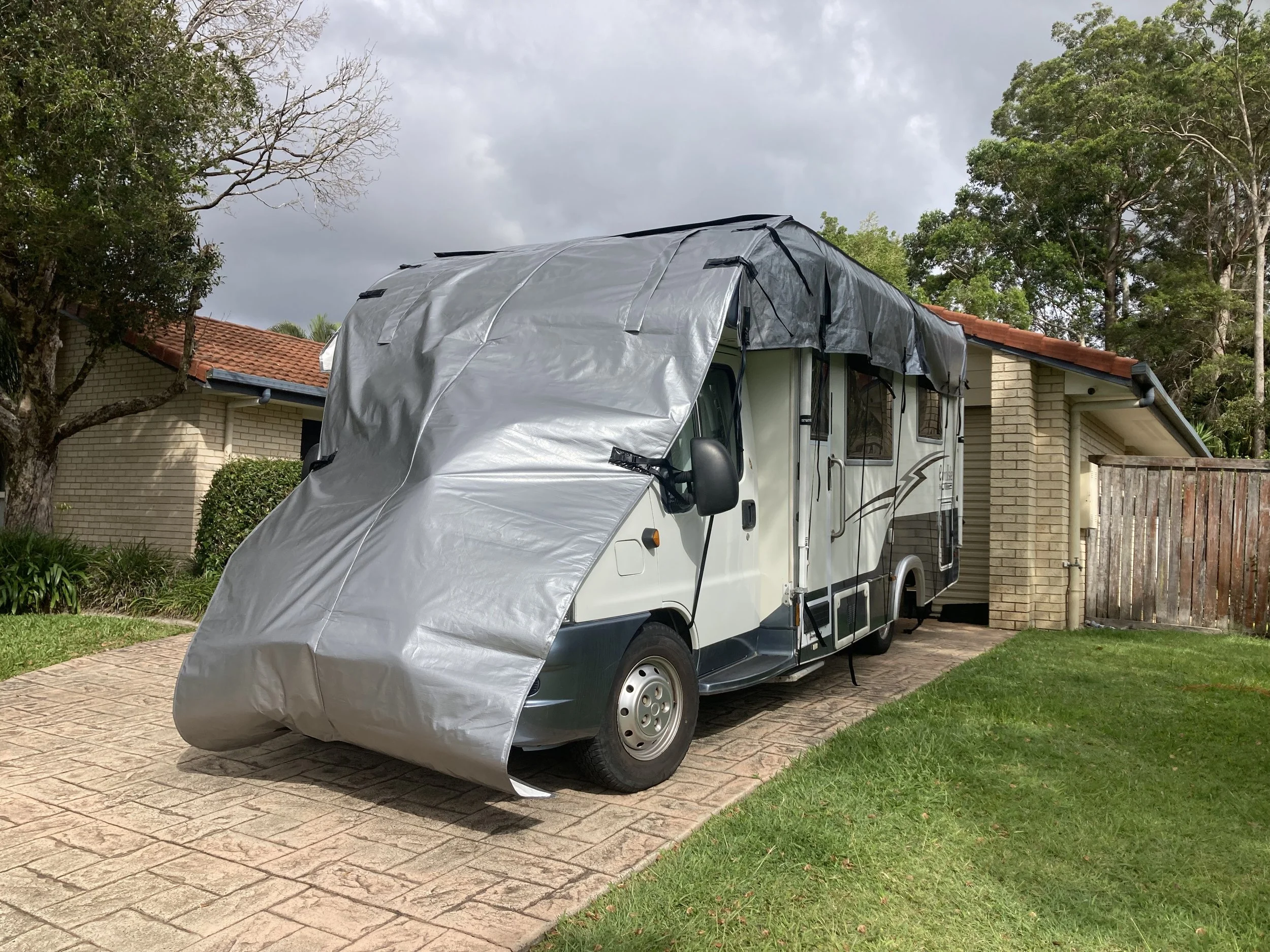A camper van parked in a driveway with its cover partially removed, exposing the front and side of the vehicle.