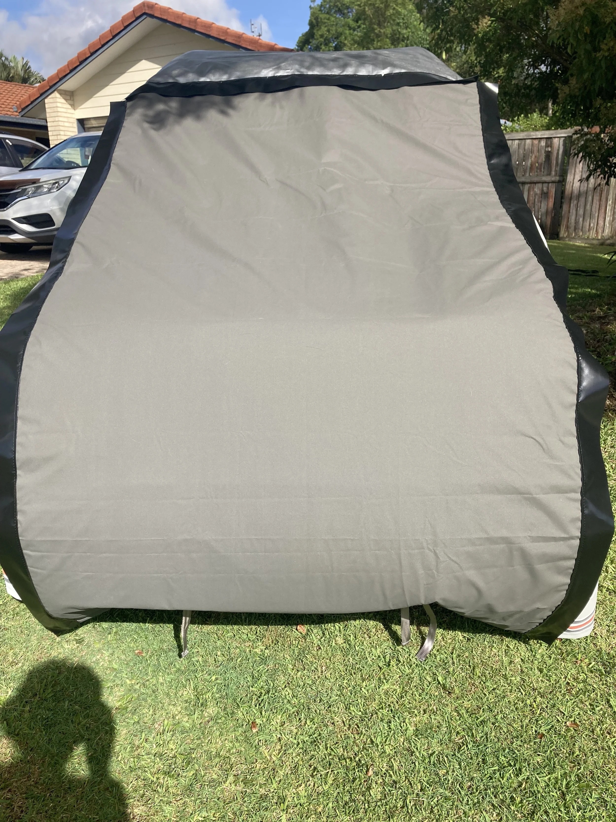 A gray outdoor Hamilot Cover on a 4WD on a grassy area in a backyard with a house, cars, and trees in the background.