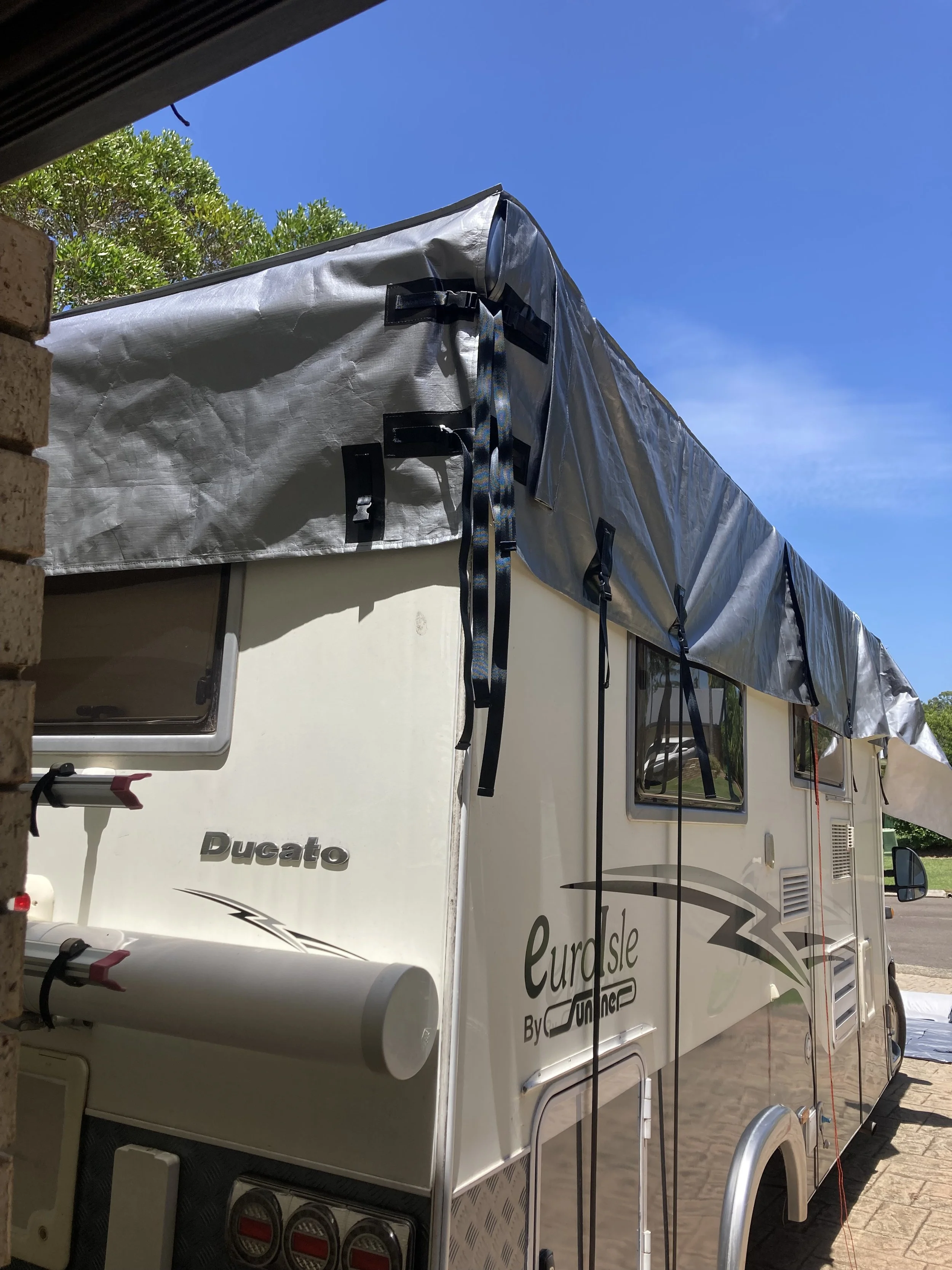 A motorhome with a grey Hamilot cover on the street against a blue sky.