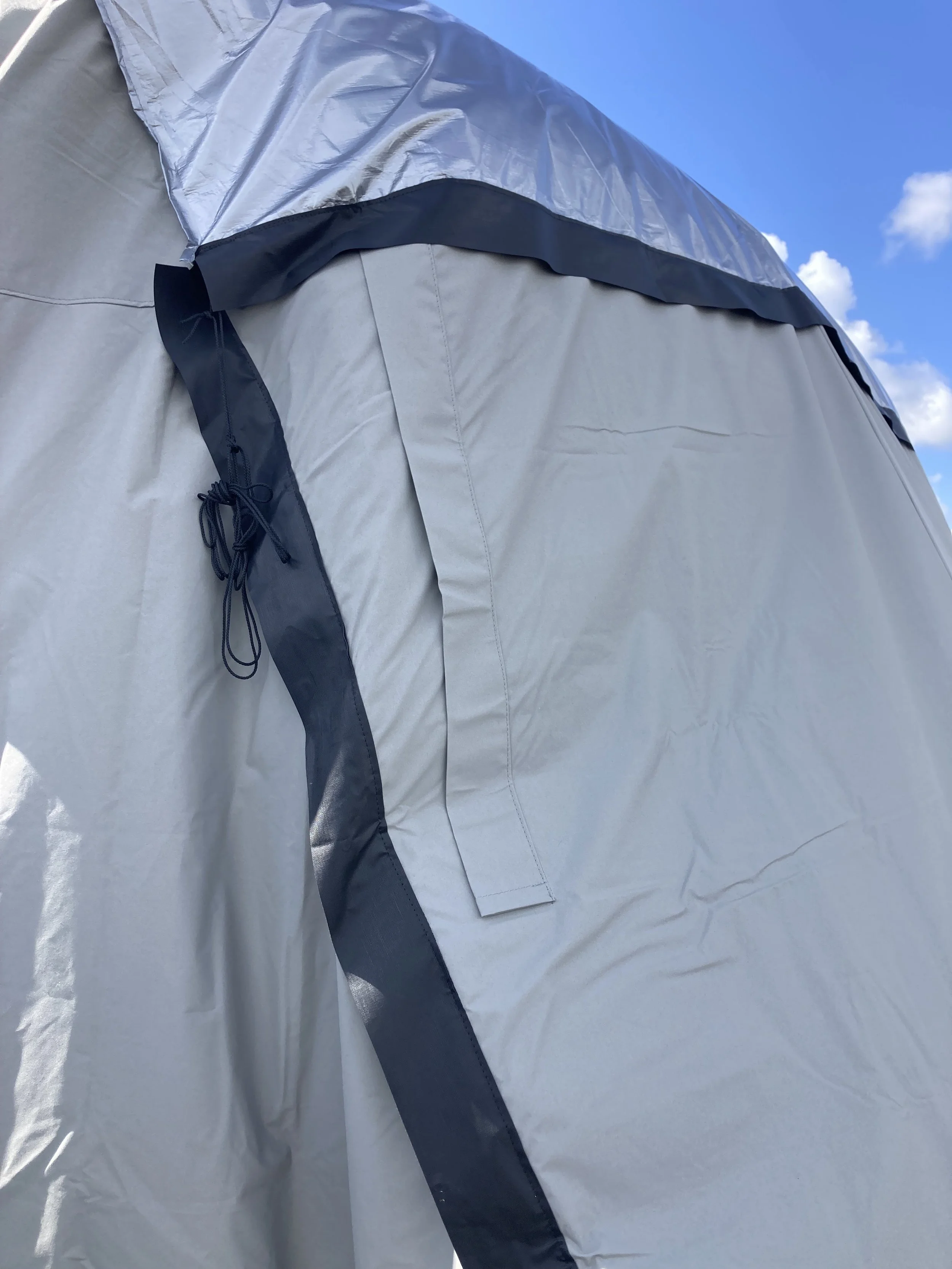Close-up of a gray outdoor tent with black trim, set against a blue sky with some clouds.
