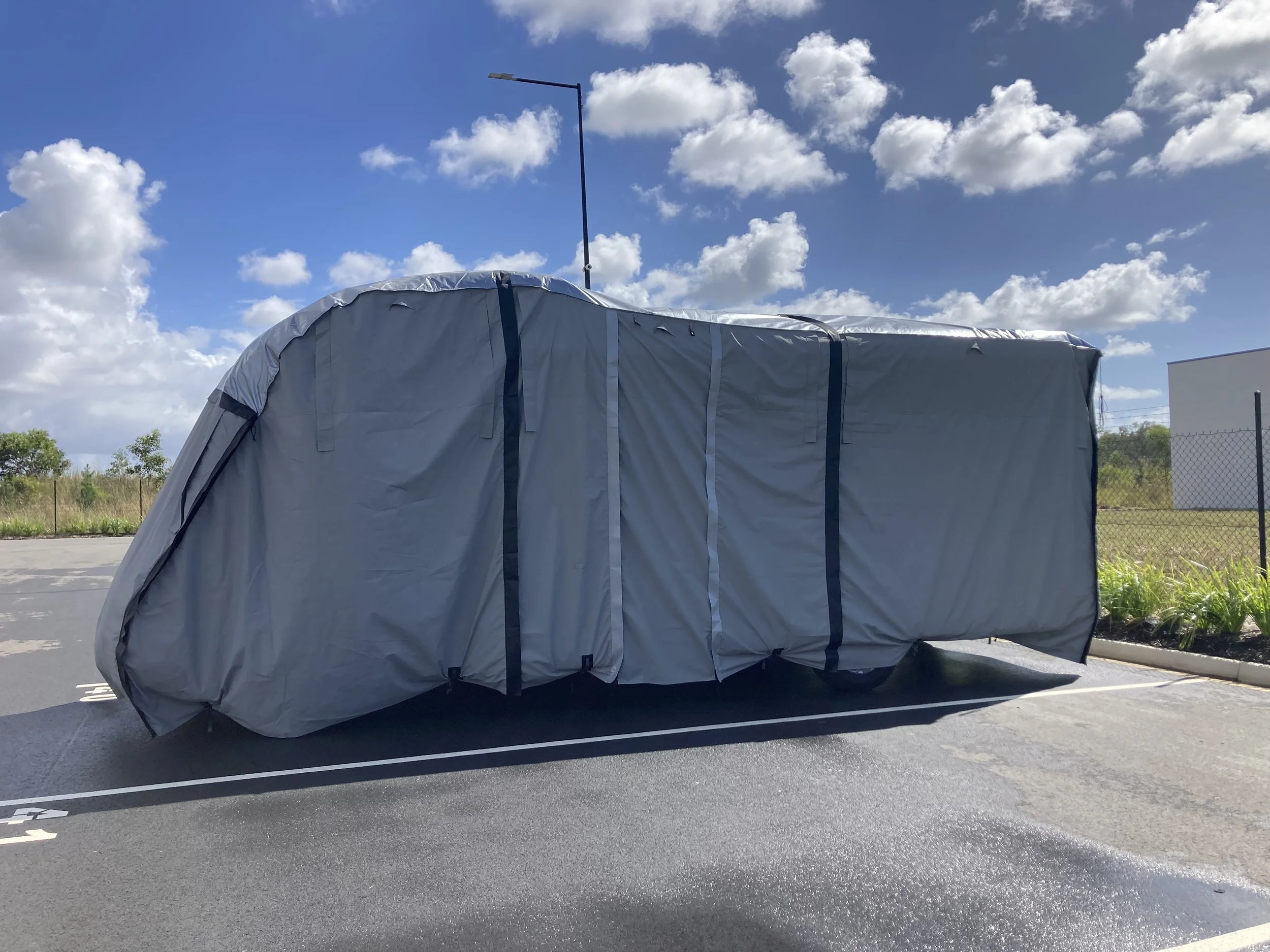 A parked Euro Isle camper van on a paved driveway with a clear blue sky and some trees and houses in the background.