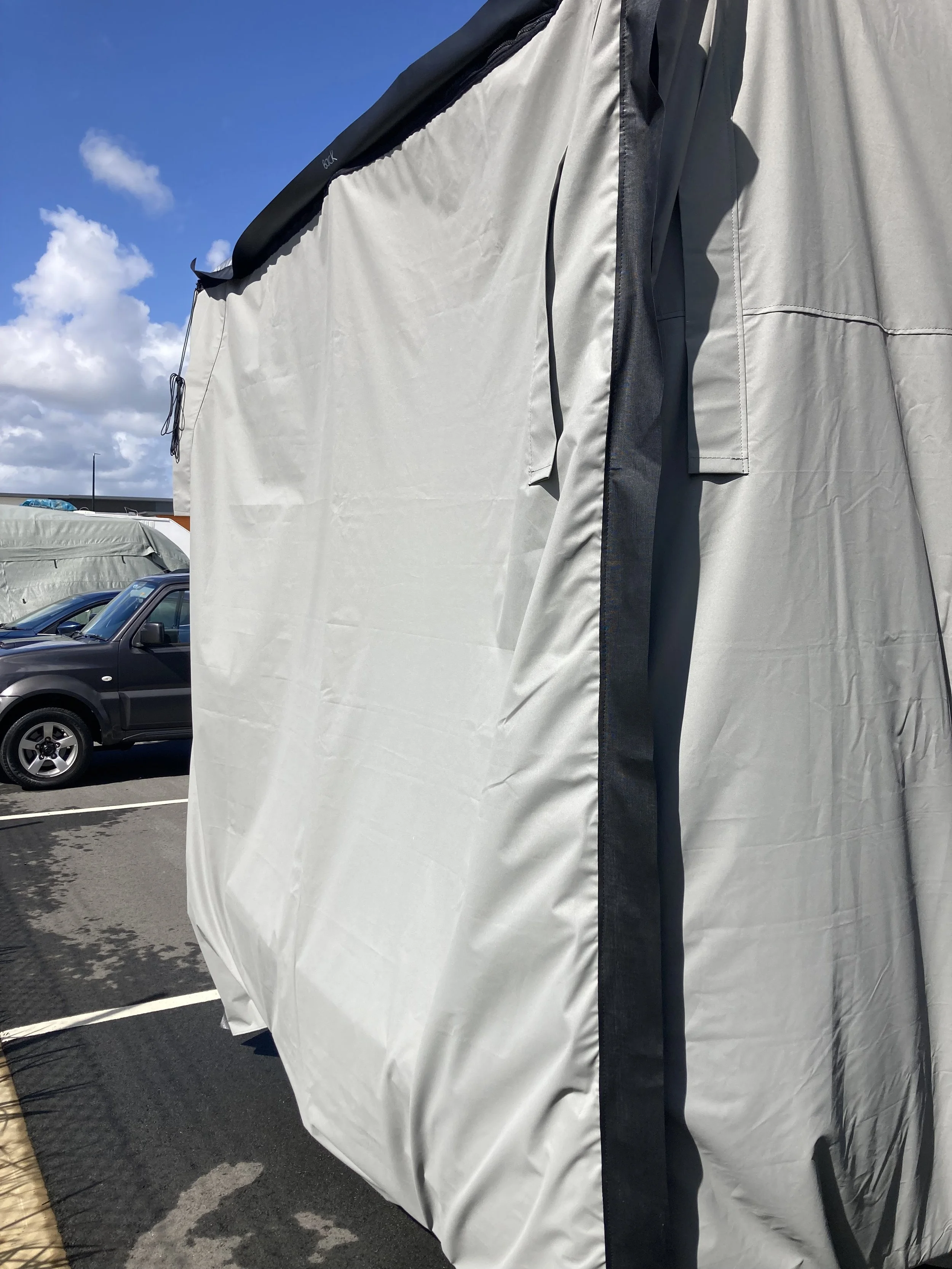 A Hamilot cover protecting a large caravan parked outdoors under a blue sky.