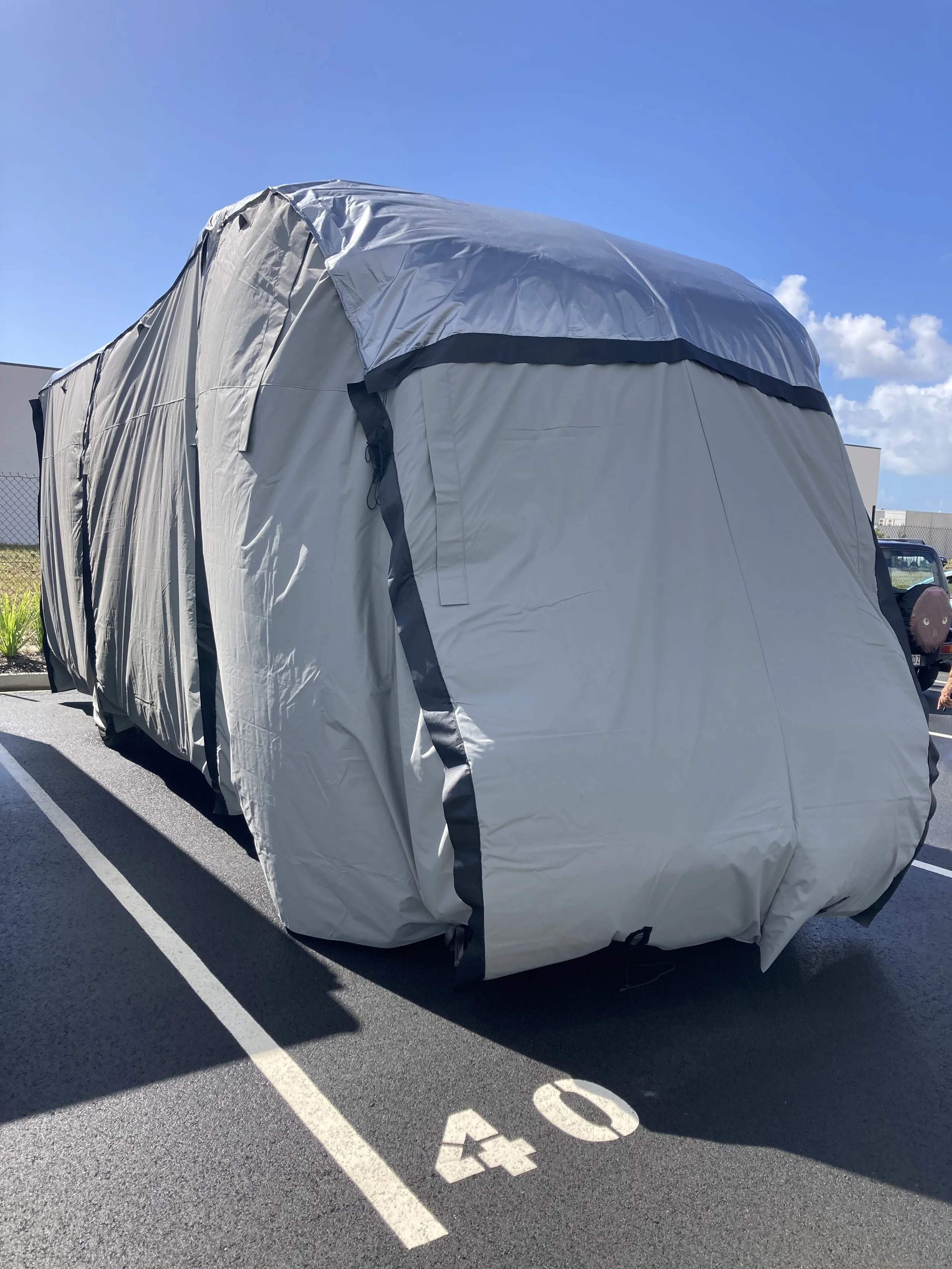 Angled front view of a caravan protected by a Hamilot hail cover in a parking bay.